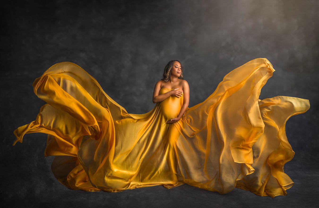 Best Maternity Photographer CT pregnant woman with a gold cloth sweeping out from her body in a dramatic way for a maternity photograph