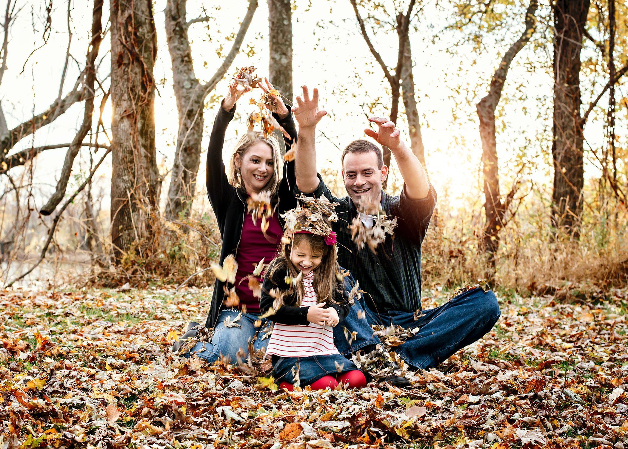 Mom and Dad shower their young daughter with fall leaves