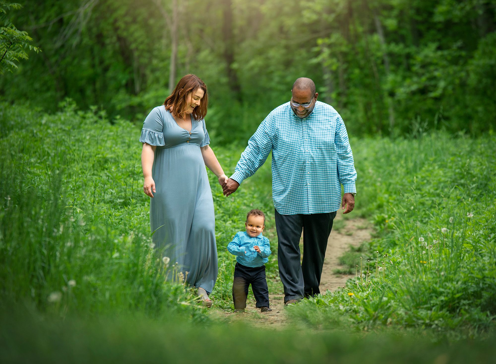 Family Photographers in CT couple holding hands walking down path in the woods with their one year old son