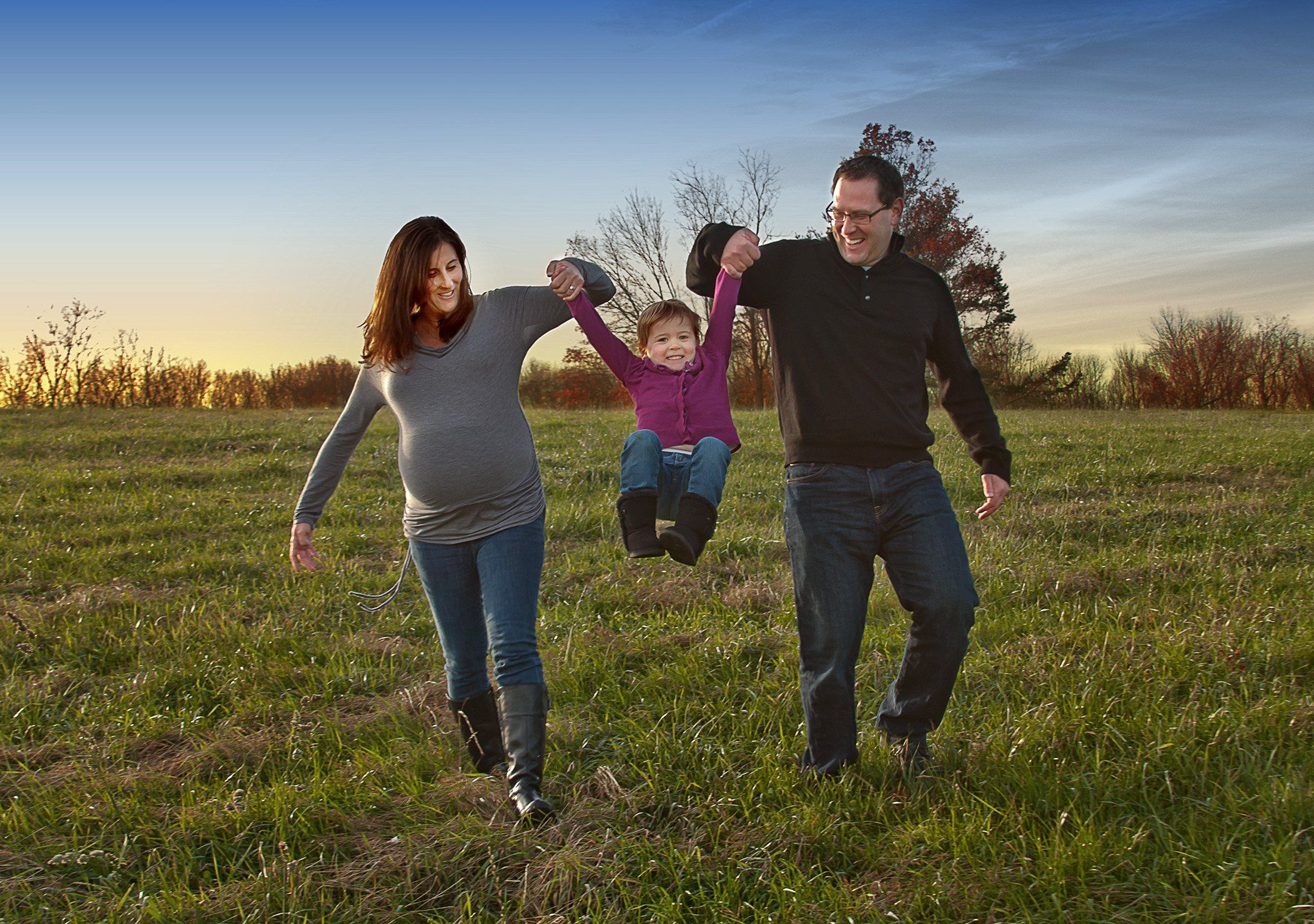 Pregnant Mom and Dad swinging 2 year old between them while walking at sunset