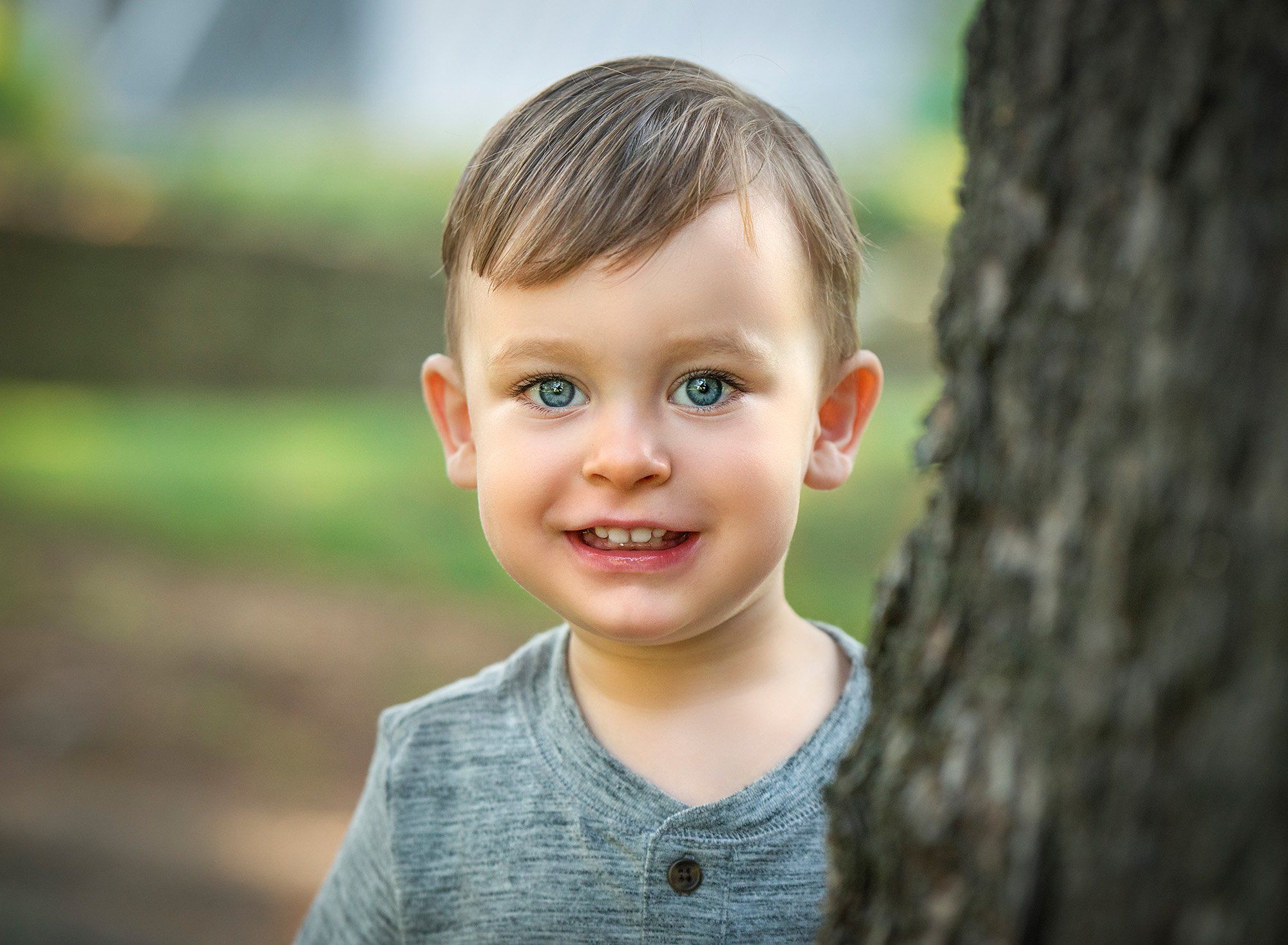 two year old boy smiling behind a tree