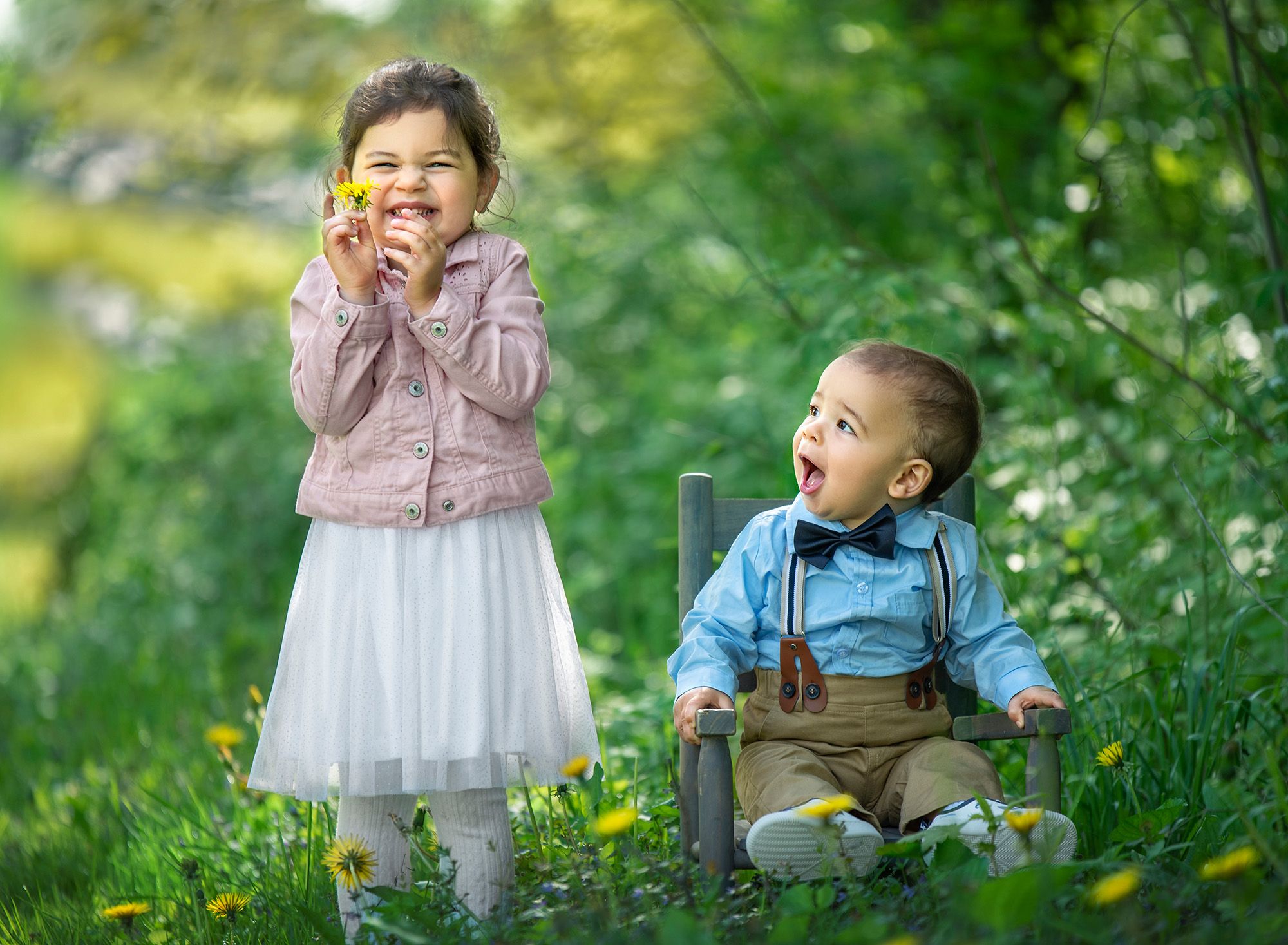 CT Family Photographer young girl smiling while holding a dandelion as younger brother smiles in awe while sitting in a rustic chair beside her