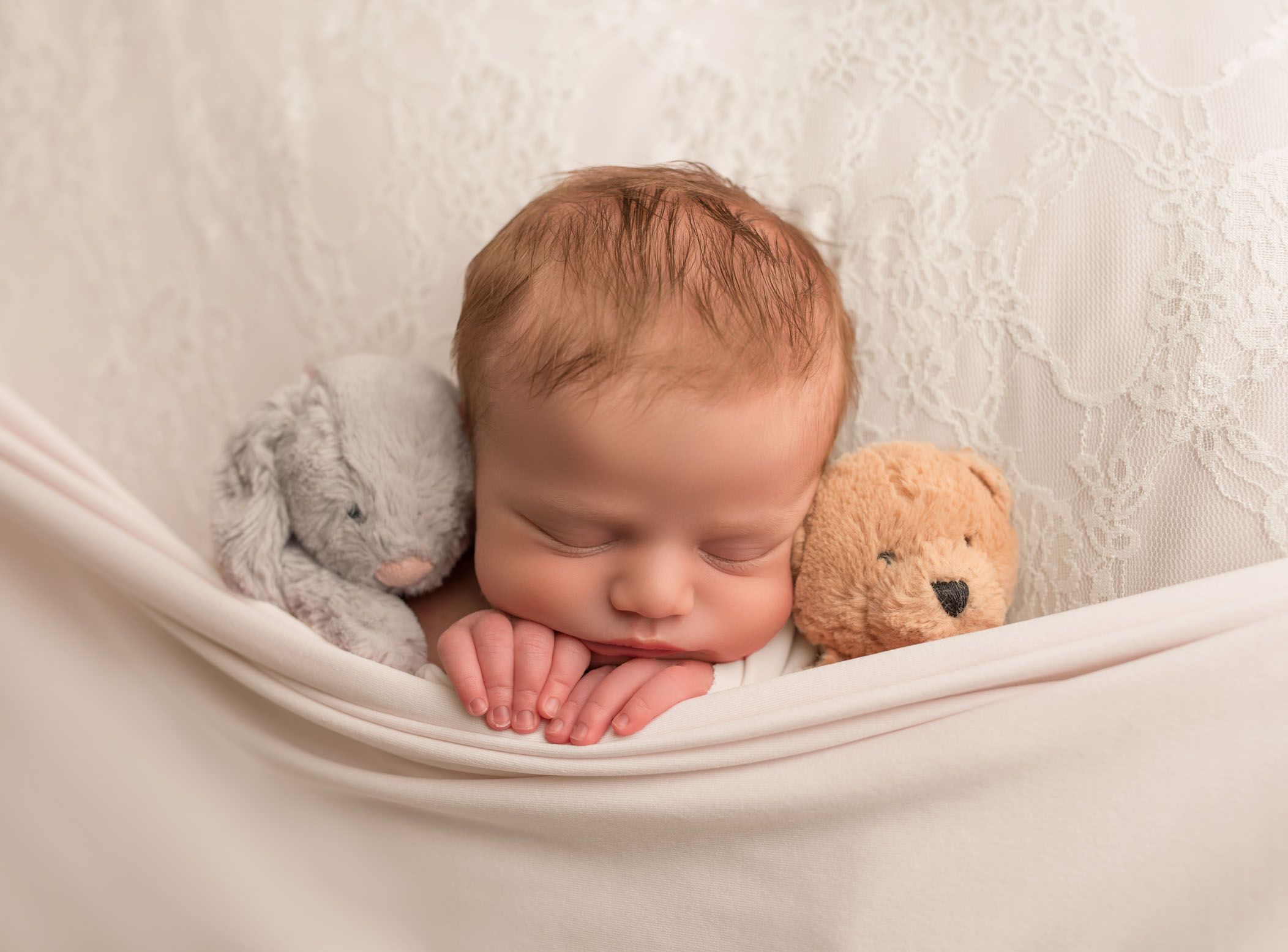 newborn bay girl tucked into sleep with her stuffed animals