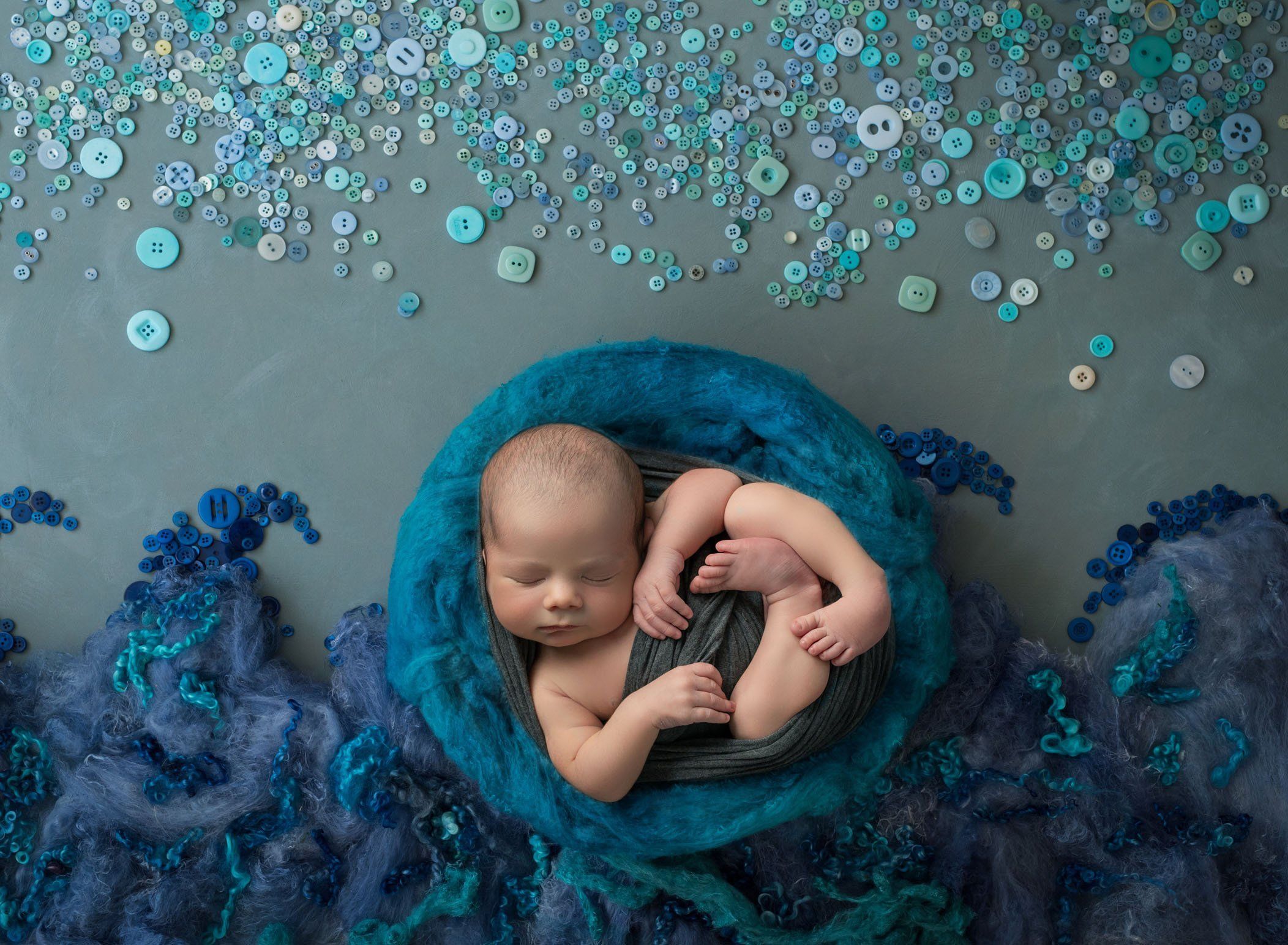 newborn baby boy sleeping in blue wool nest with fabric made waves and a button made sky newborn baby boy sleeping in blue wool nest with fabric made waves and a button made sky
