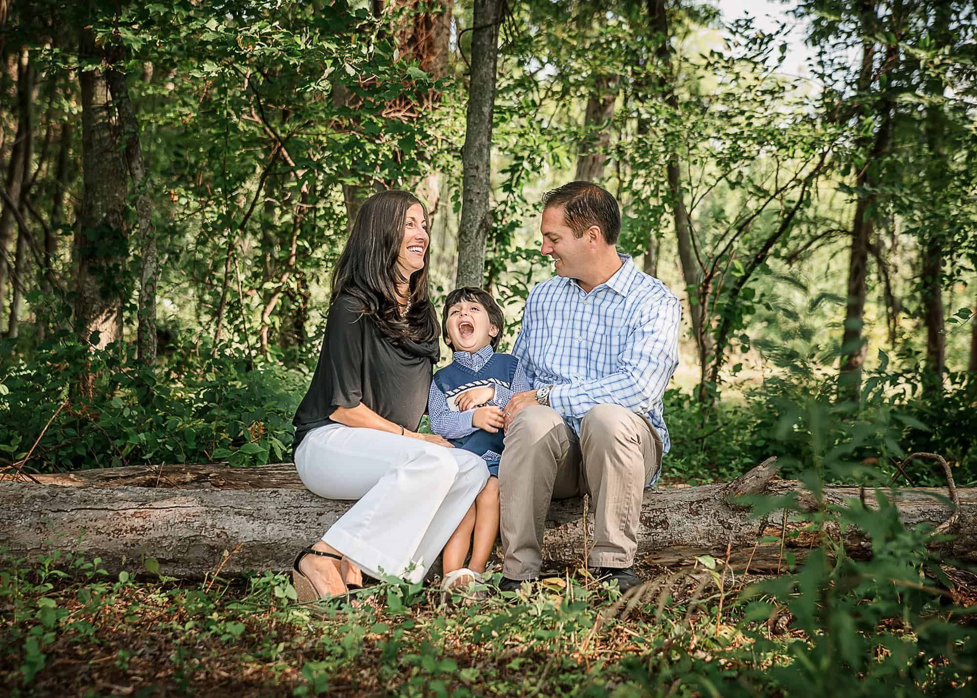 family of 3 sitting on a log in the forest in summer sharing a laugh