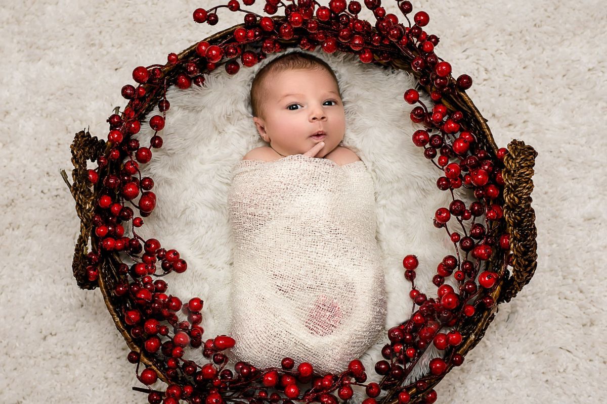 newborn baby wrapped in white blanket lying in a basket surrounded by christmas berries Glastonbury CT Newborn Photographer One Big Happy Photo www.onebighappyphoto.com/newborns