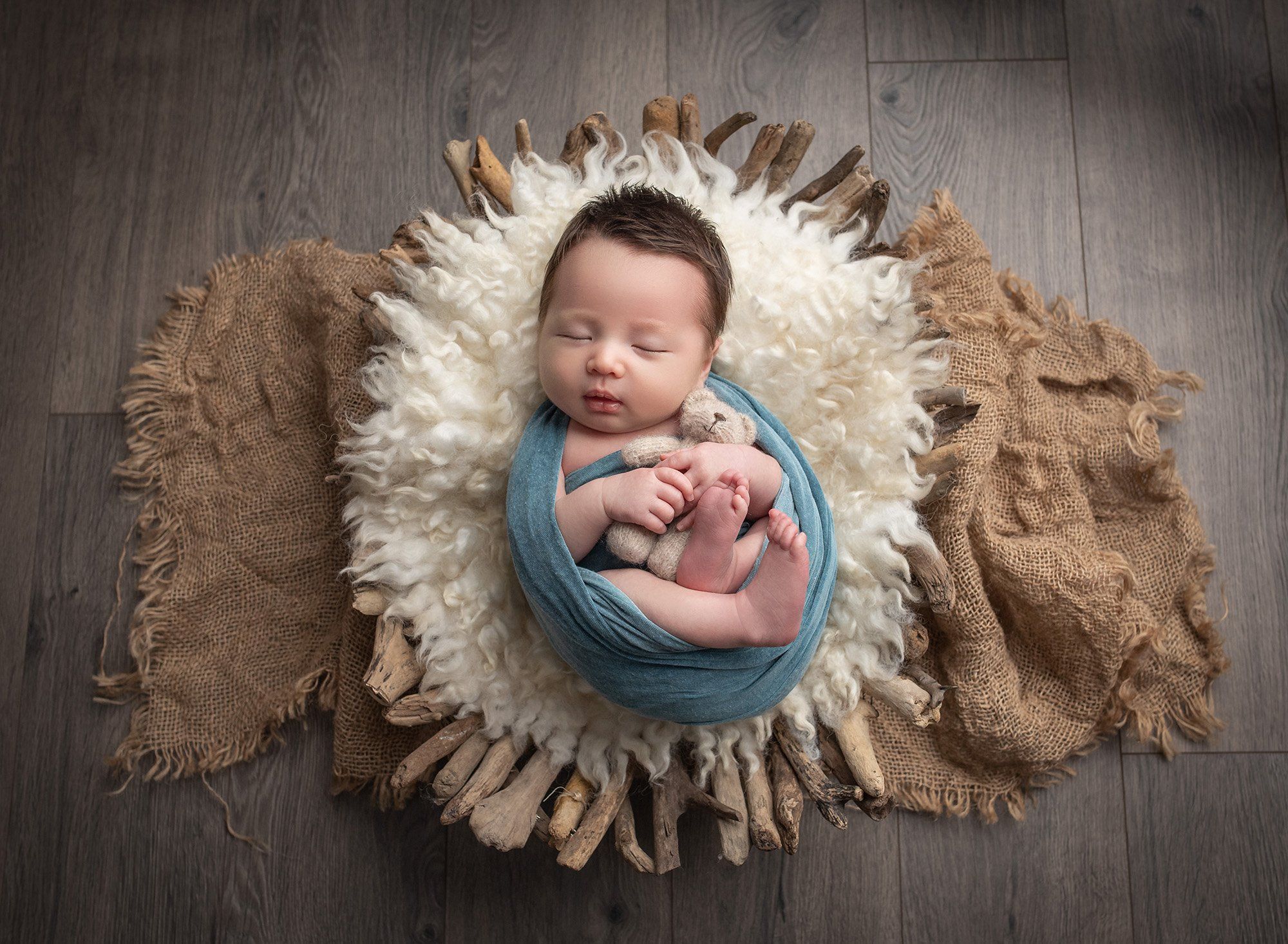 newborn baby boy swaddled in teal with his teddy bear in a driftwood bowl best time to take newborn photos