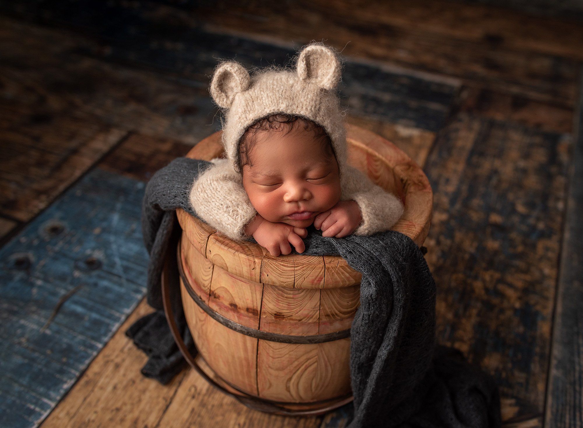 black newborn baby boy sleeping in a wooden bucket wearing a knitted teddy bear romper best time to take newborn photos