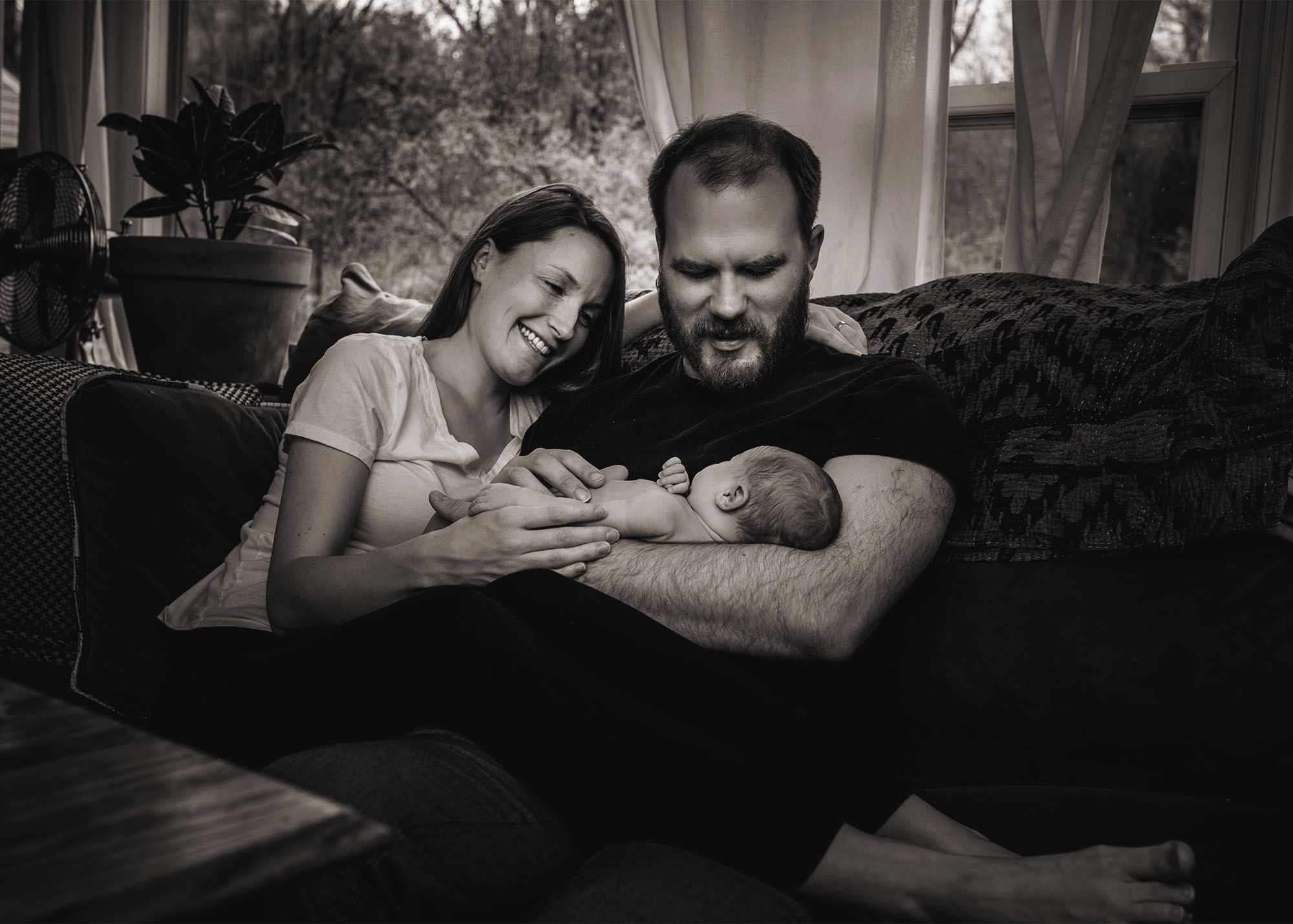 Dad holds newborn on the couch with Mama smiling and looking on Glastonbury CT Newborn Photographer One Big Happy Photo www.onebighappyphoto.com/newborns