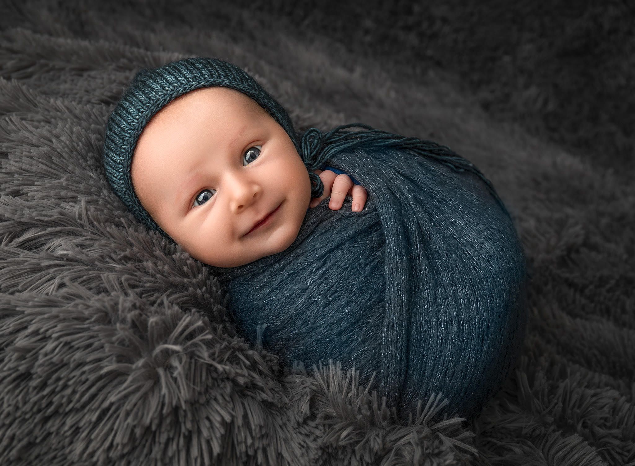 Baby boy wrapped in a soft blanket and bonnet, looking toward the camera