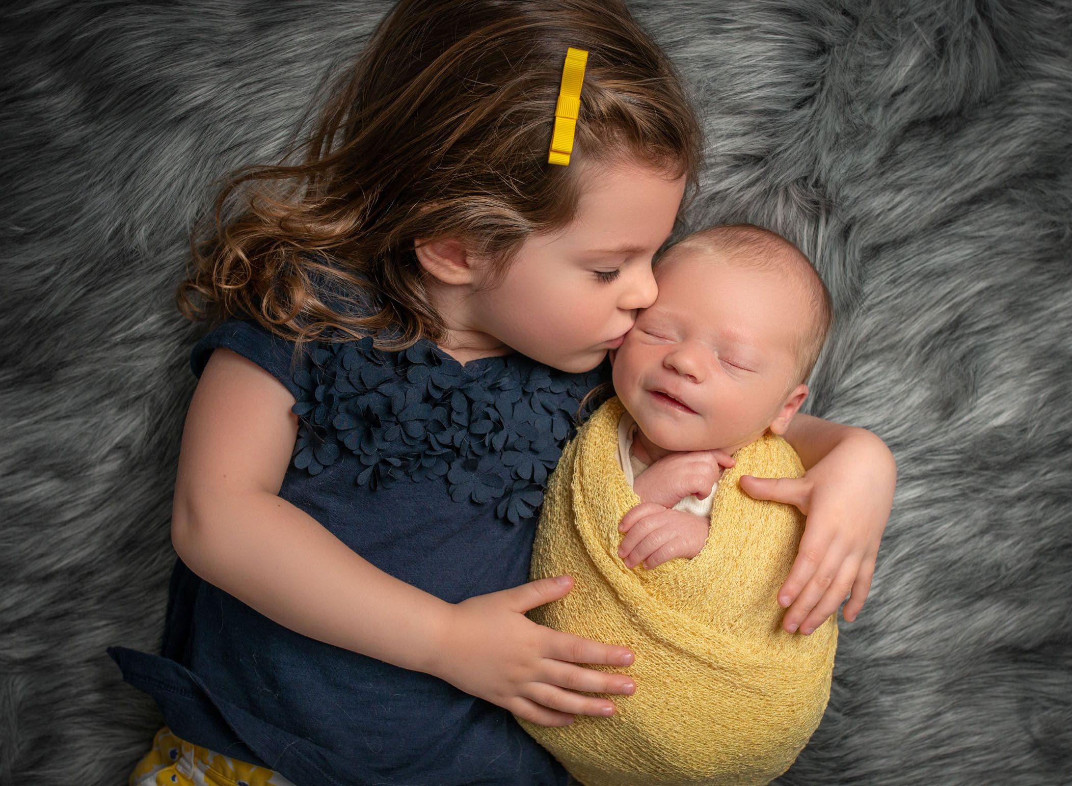 3 year old big sister kissing smiling newborn baby