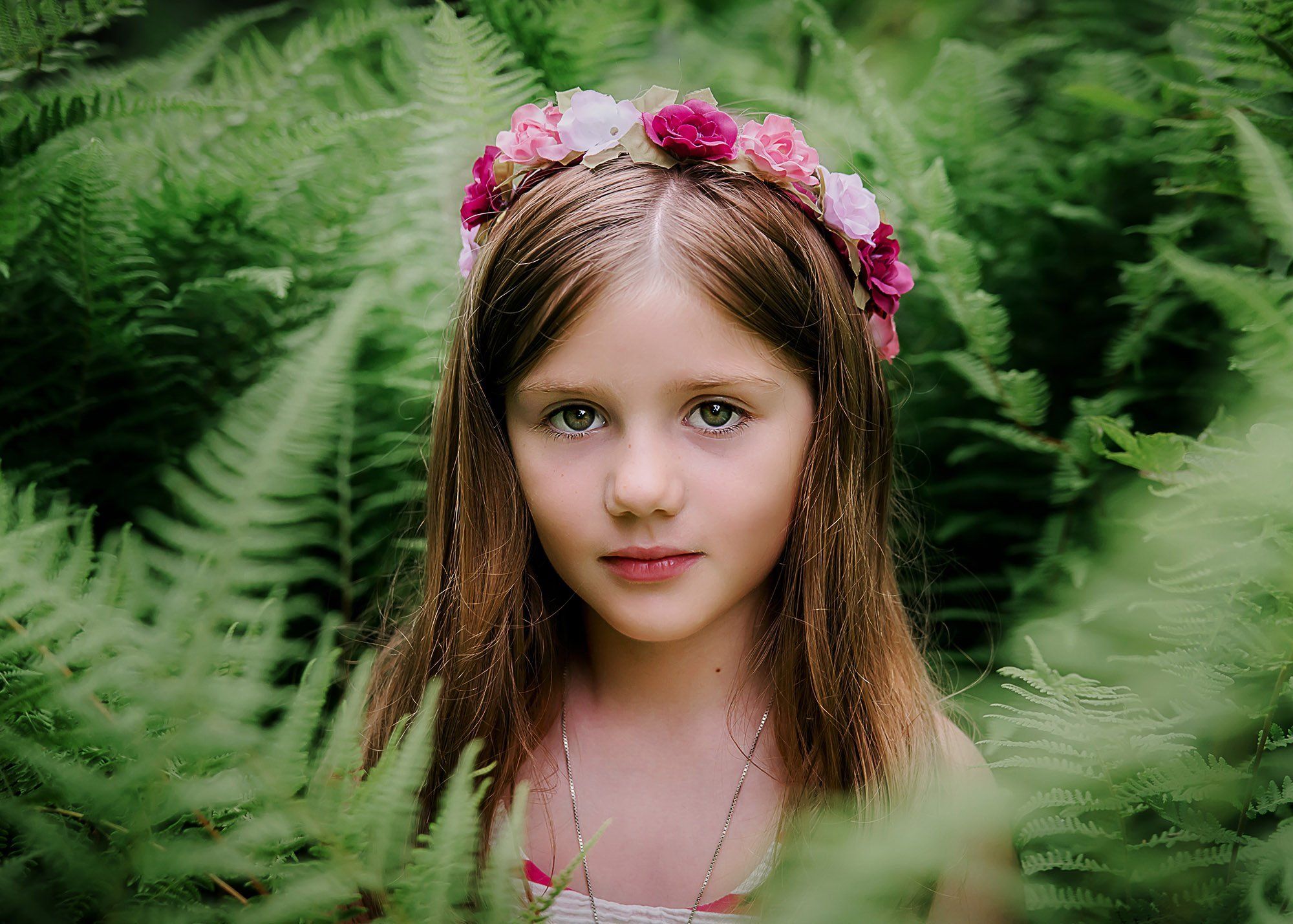 little girl sitting in a bed of ferns with a floral crown on her head