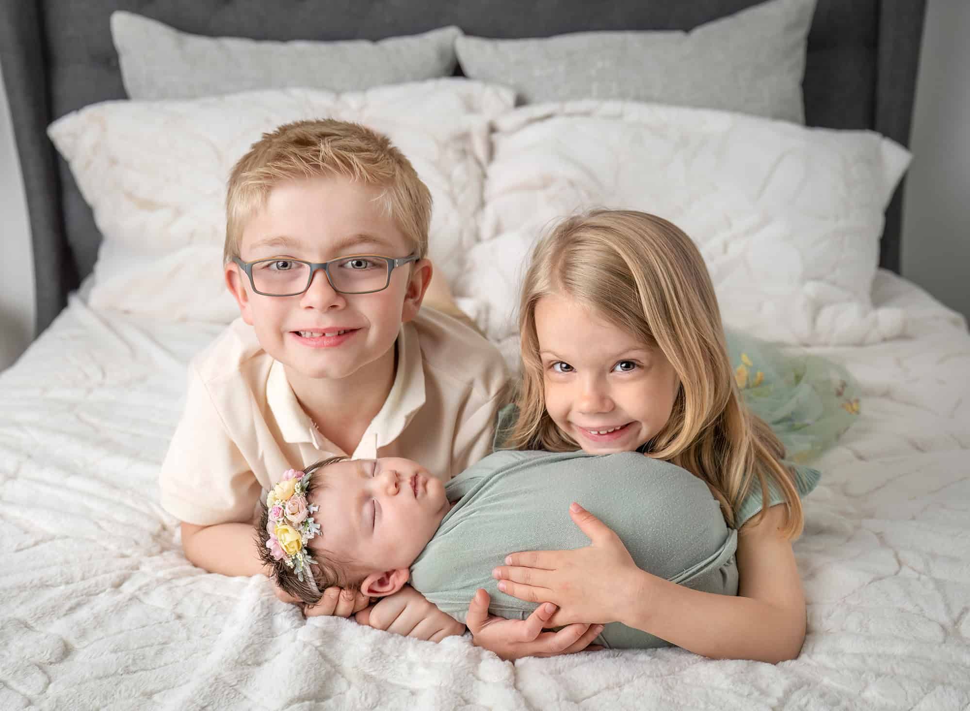 newborn photos with siblings — siblings snuggling newborn on bed at studio