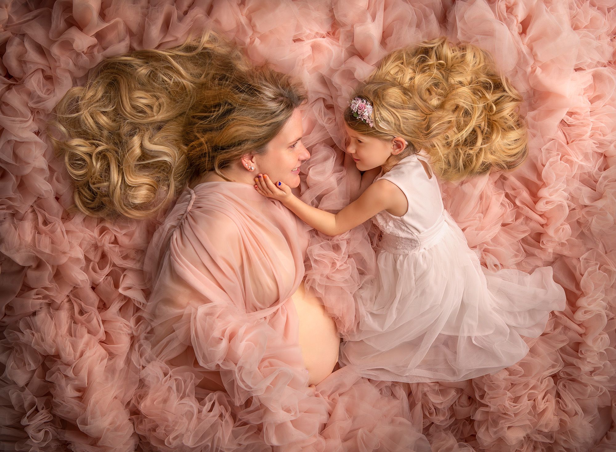 maternity and newborn photographer mom and big sister laying on pink fluffy gown gazing at each other with smiles