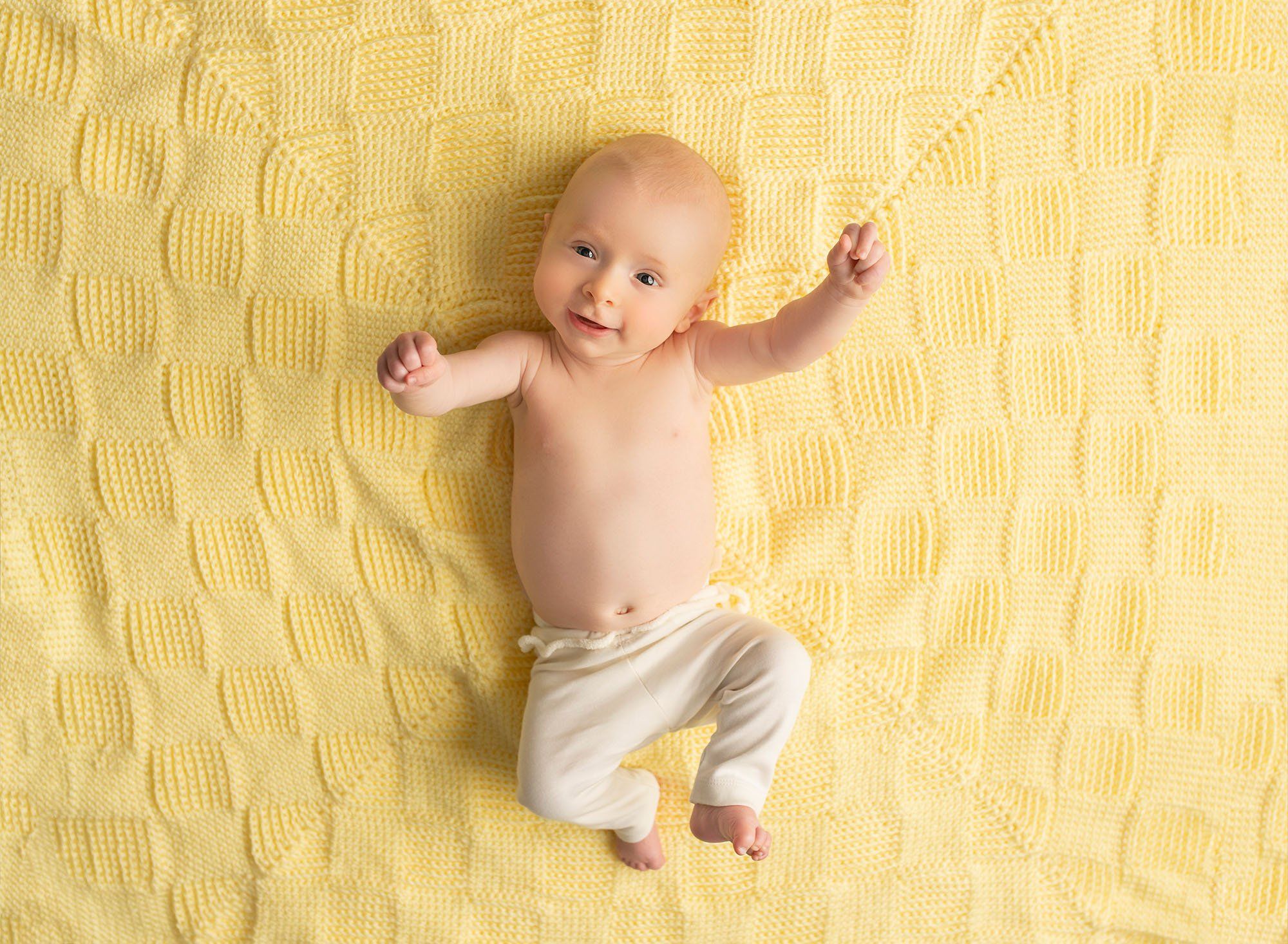 3 month old baby boy stretching on yellow blanket and looking at the camera