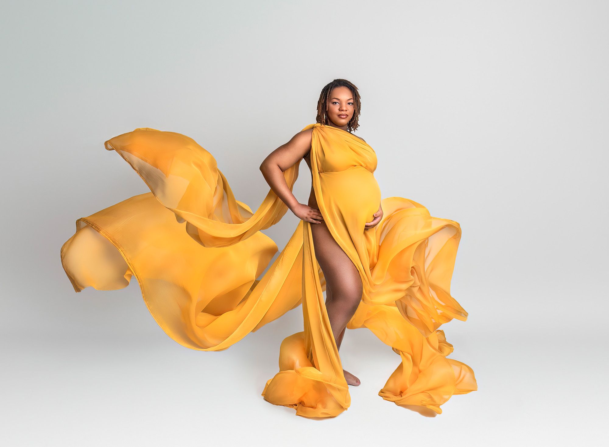 Maternity and Newborn Photographer Pregnant woman wearing gold flowing fabric on a white background