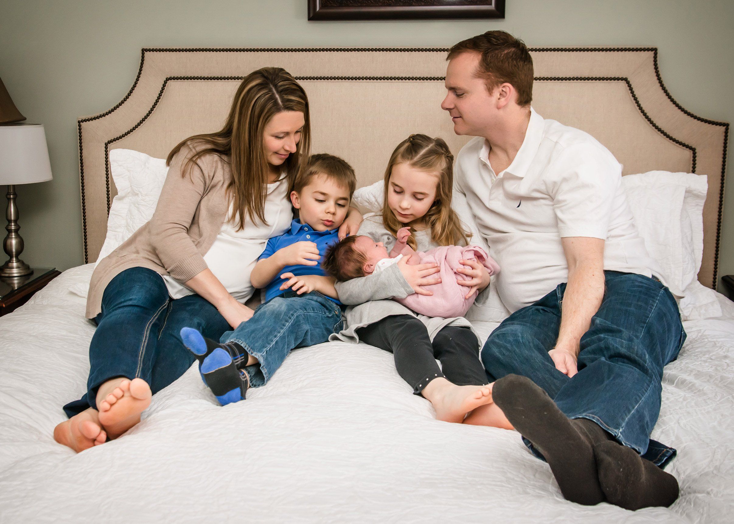 Mom and Dad with 3 kids in middle on bed holding newborn Mom and Dad with 3 kids in middle on bed holding newborn