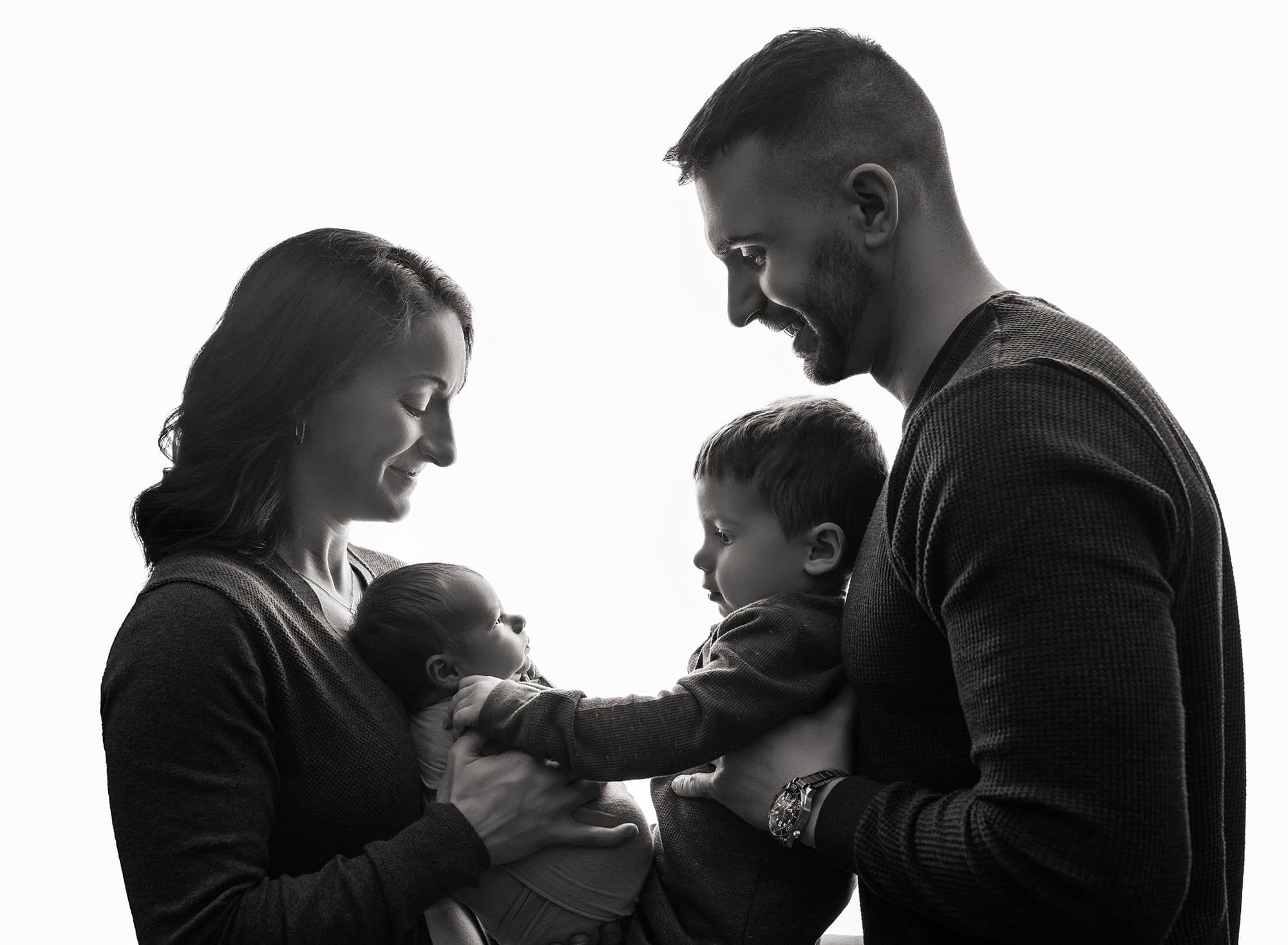 newborn brothers 2 year old gently reaches out to touch his brother's shoulder