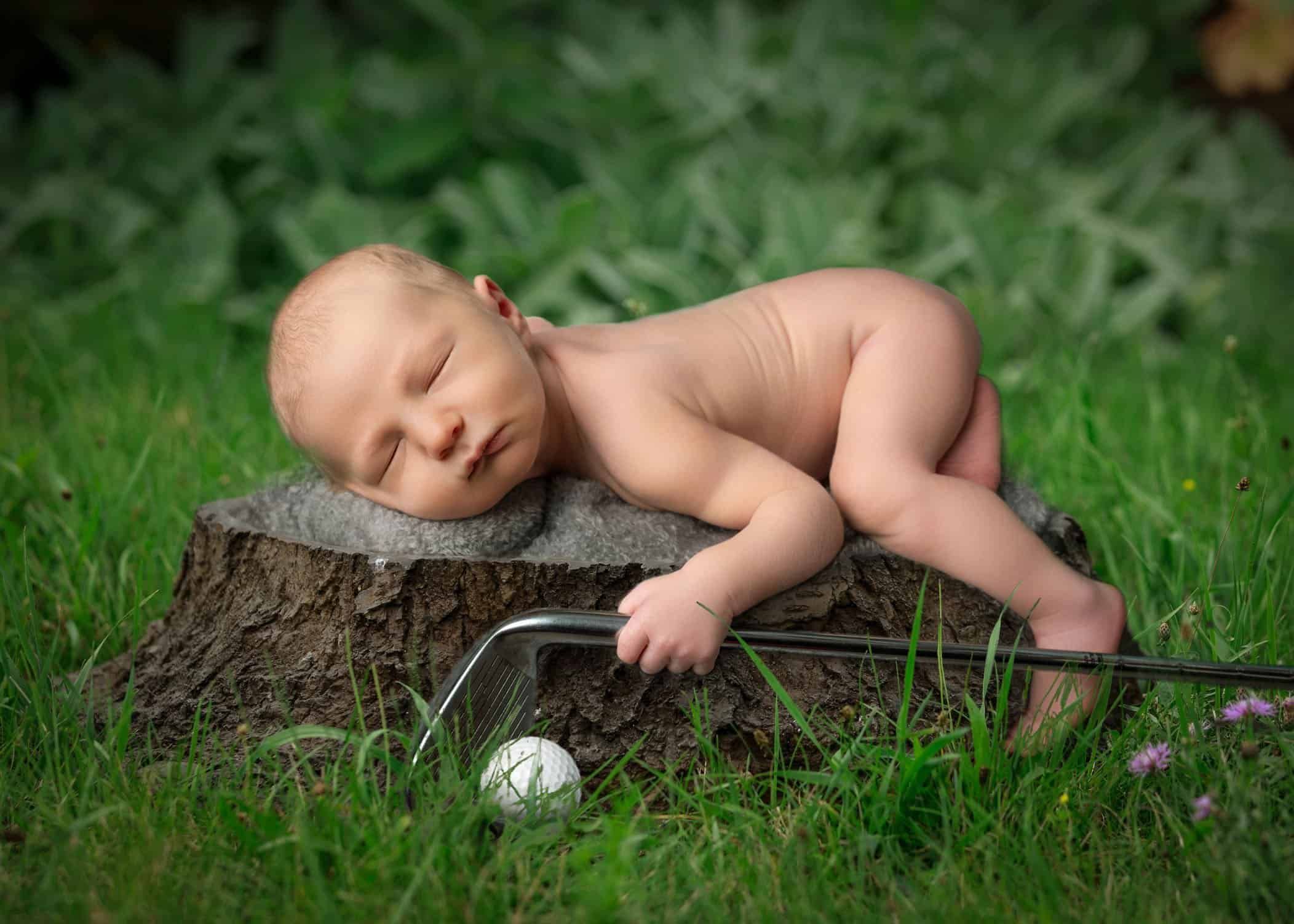 newborn boy sleeping on log outside with a golf club in his hand and golf ball below