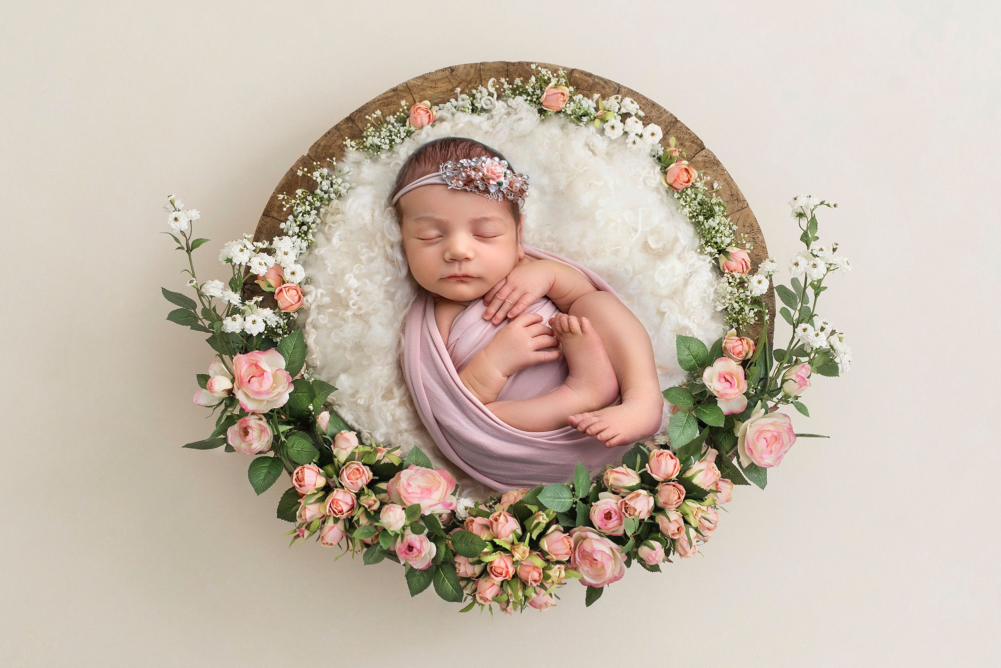professional newborn photography baby girl laying in a wooden bowl surrounded by pink roses