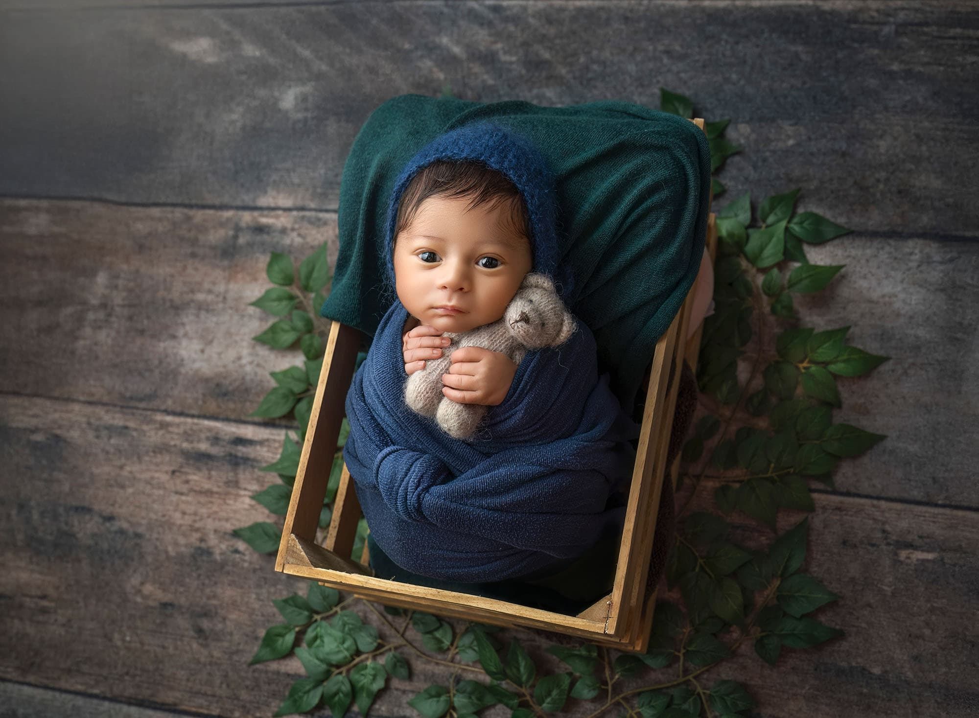 Awake newborn wrapped in navy and teal tones in wooden crate portrait