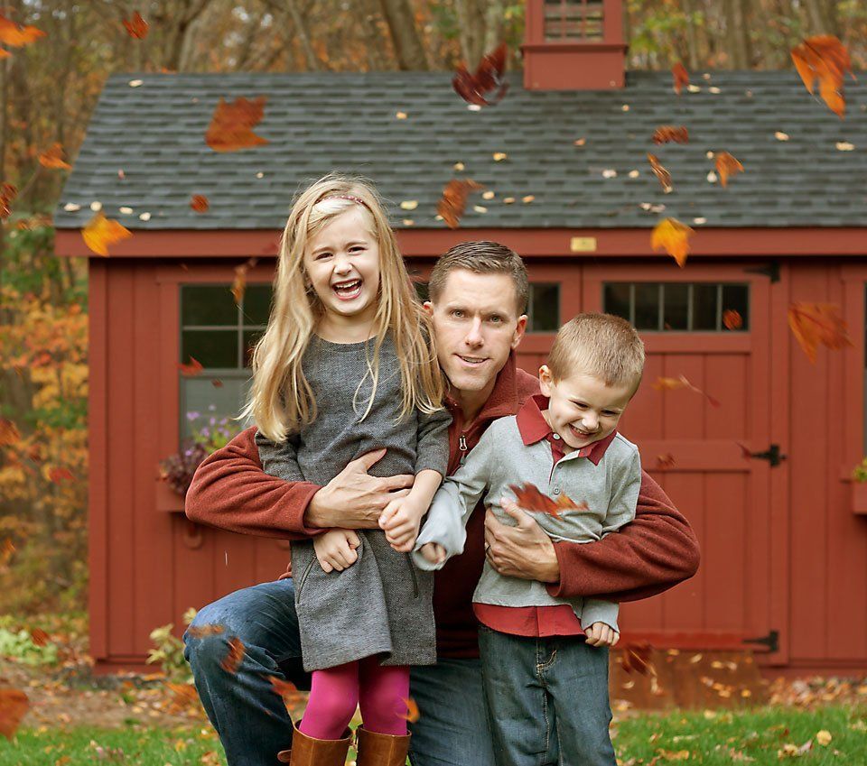 Dad plays with young daughter and young son in the falling leaves