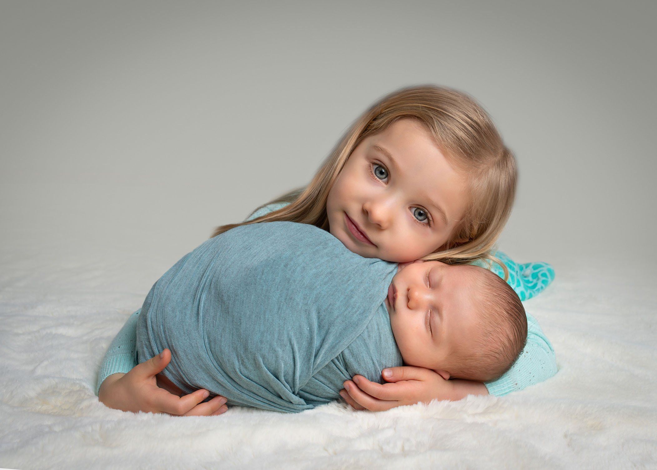 toddler girl leaning her head against newborn baby sister