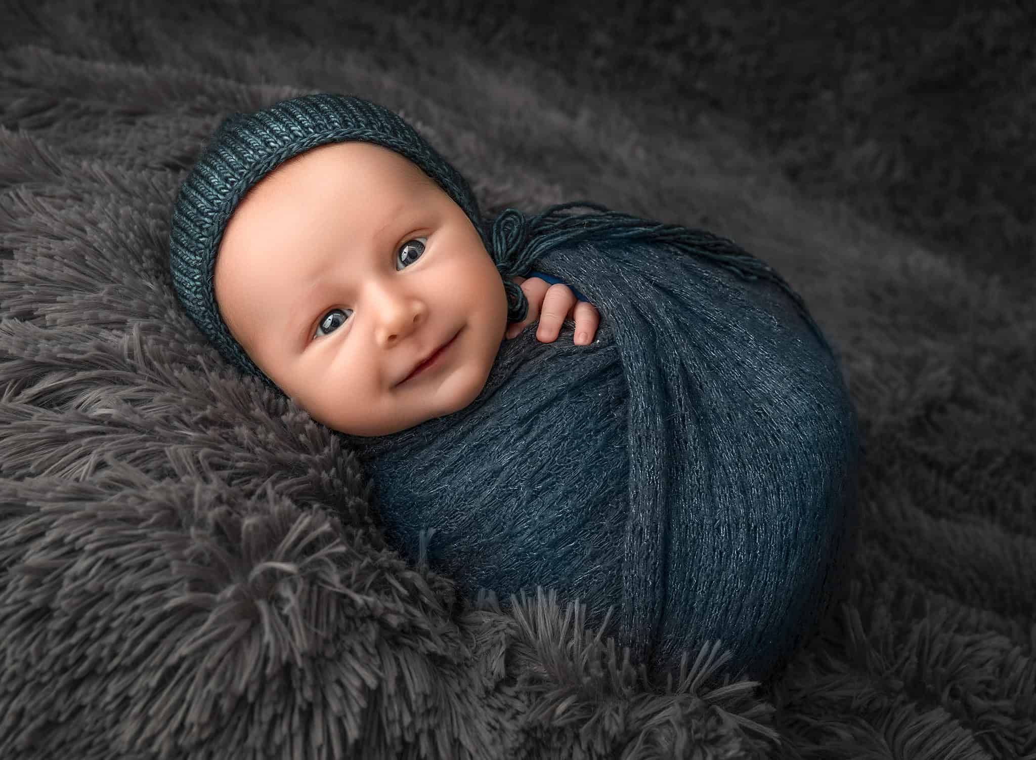 Baby boy wrapped in a soft blanket and bonnet, looking toward the camera