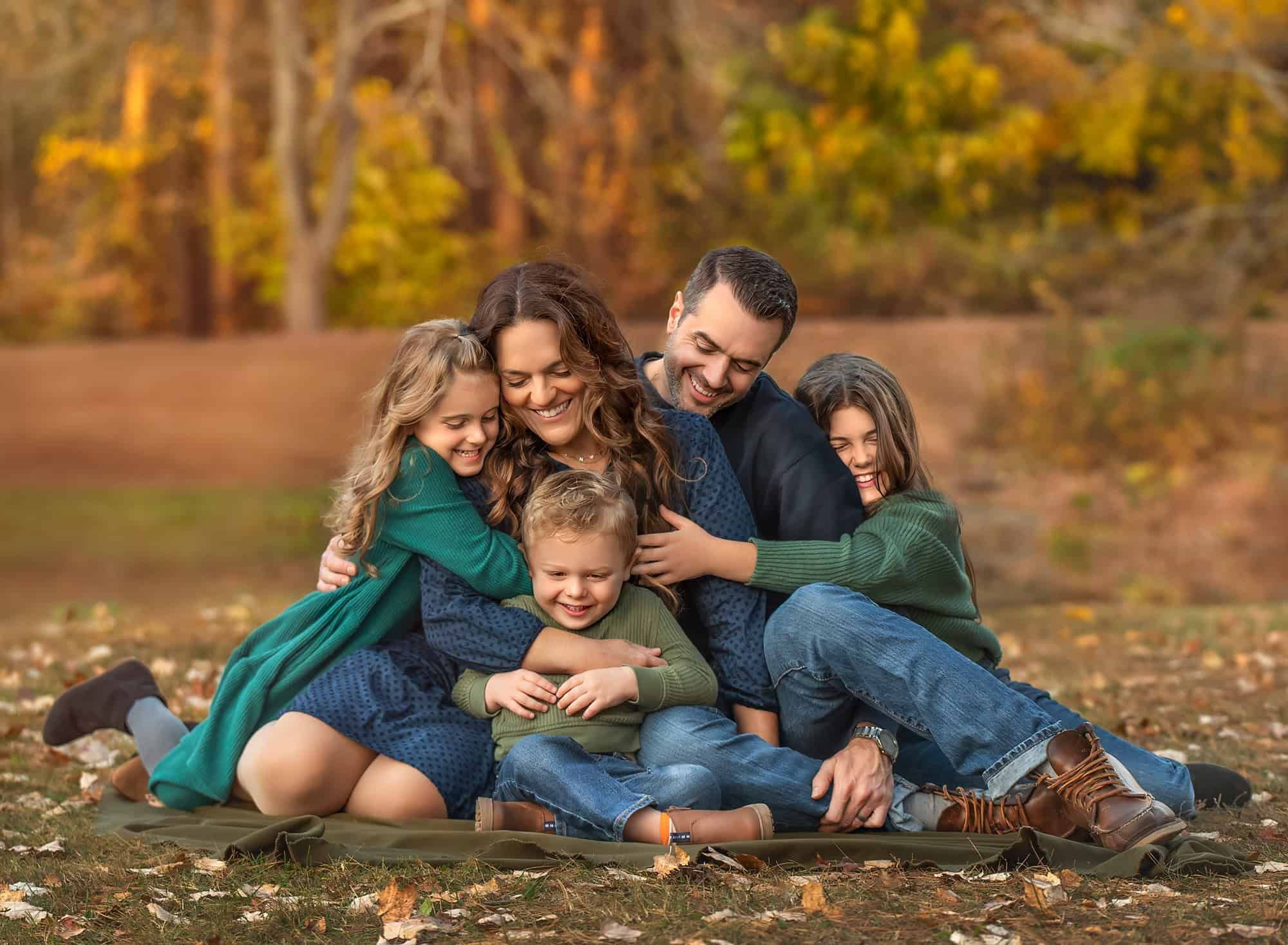 Close family cuddle on a blanket, all leaning in with eyes closed and happy smiles.