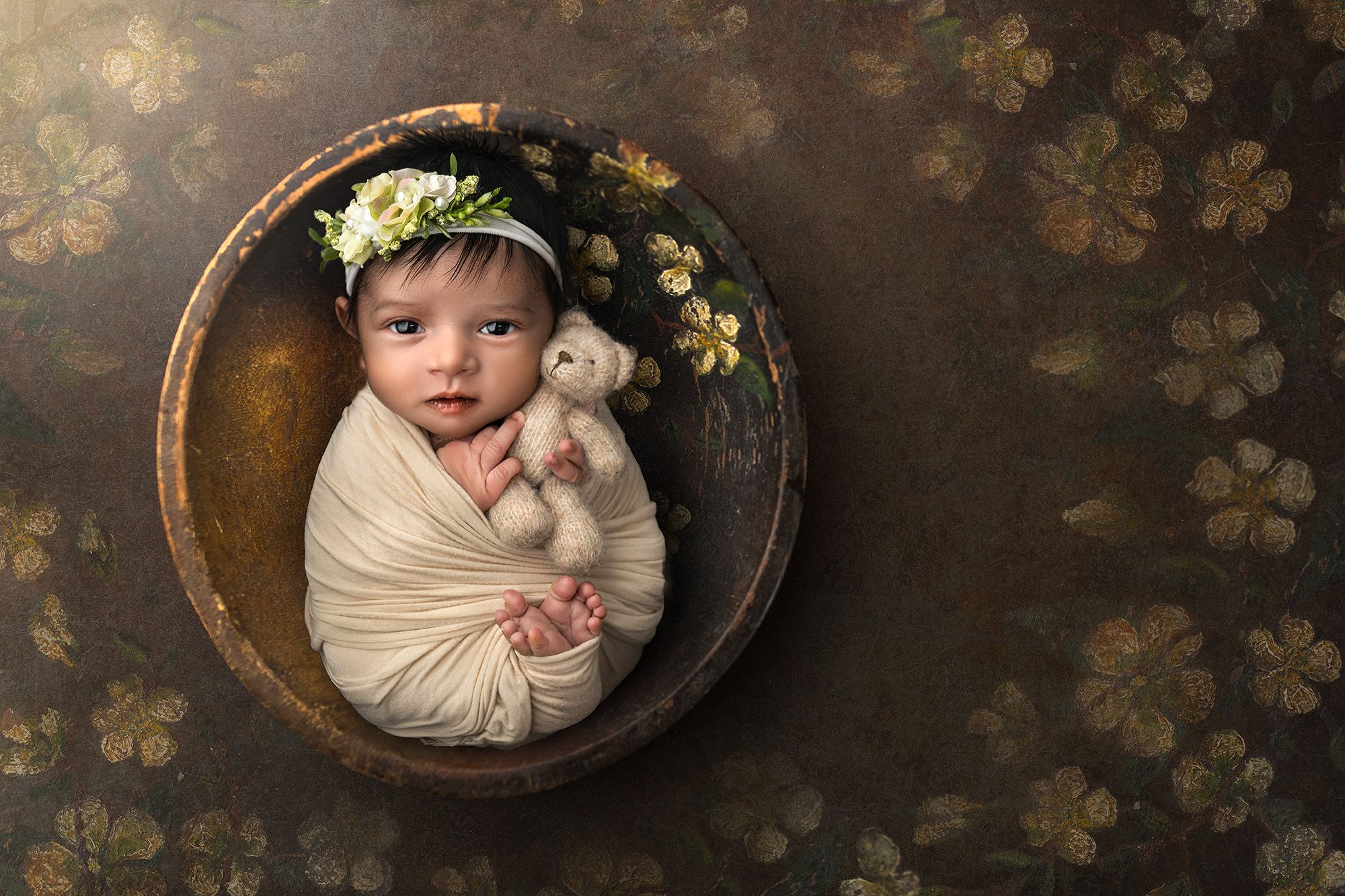 Anahita cuddling a teddy bear in a rustic bowl with gold flowers