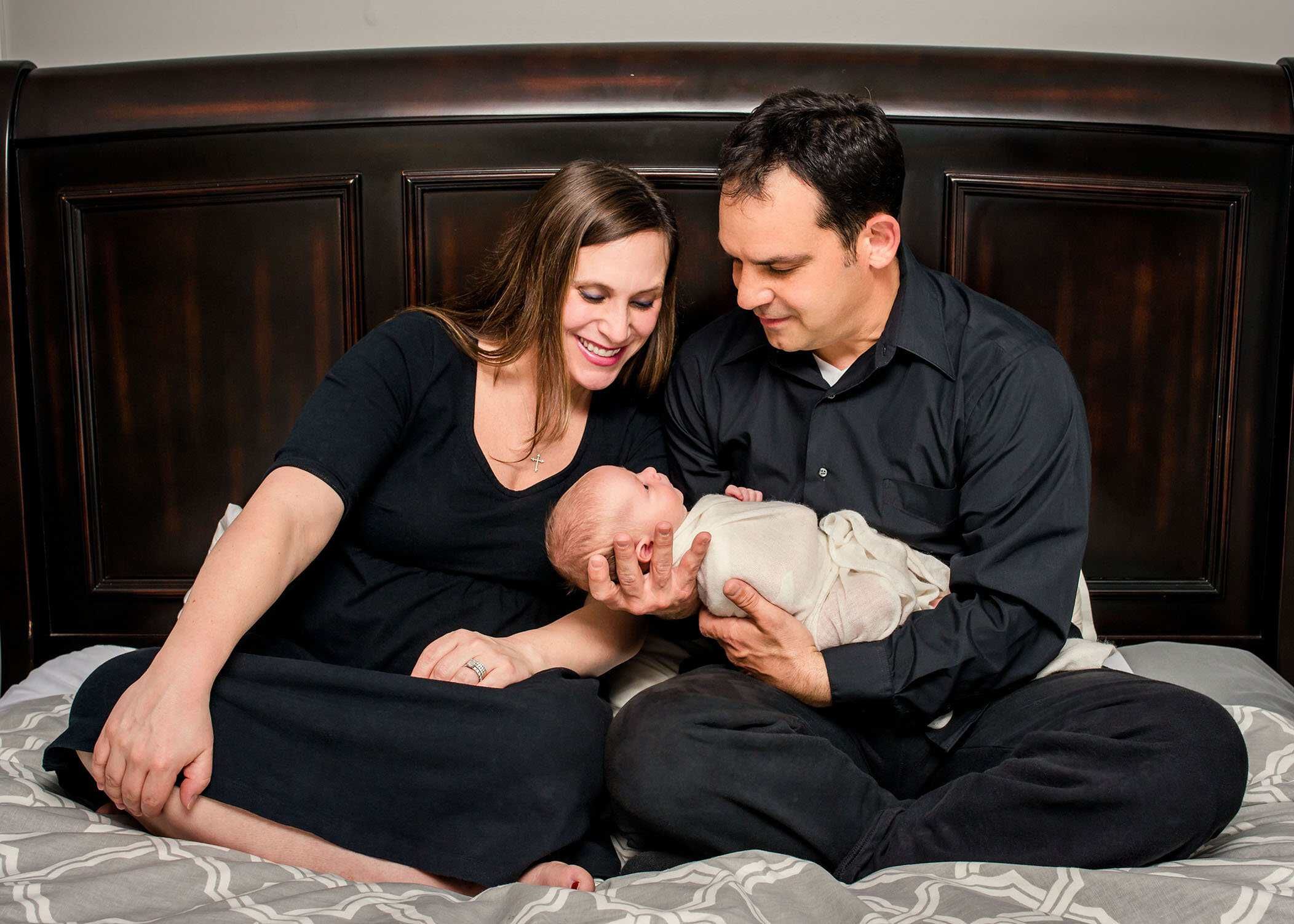 Dad and Mom holding newborn son on their bed Glastonbury CT Newborn Photographer One Big Happy Photo www.onebighappyphoto.com/newborns