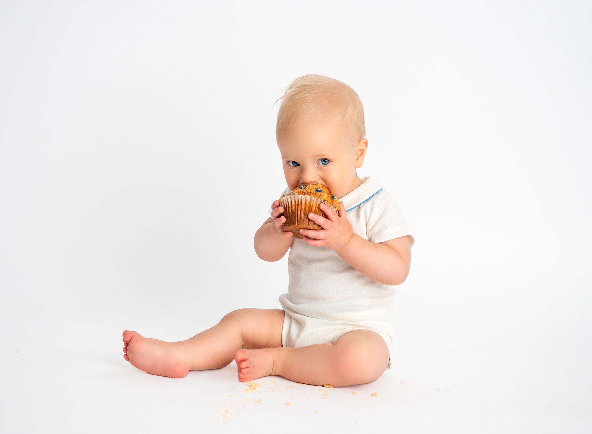 All White Baby Milestone Smash Photoshoot baby eating a blueberry muffin