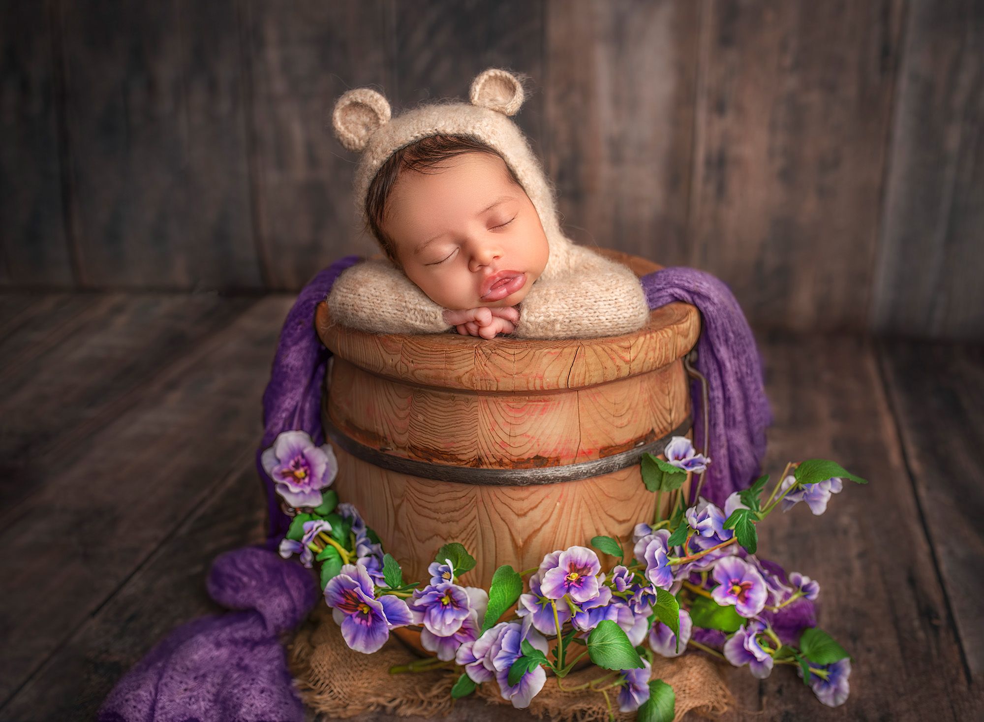 newborn photoshoot newborn baby dressed like a teddy bear asleep in a honey bucket with purple flowers