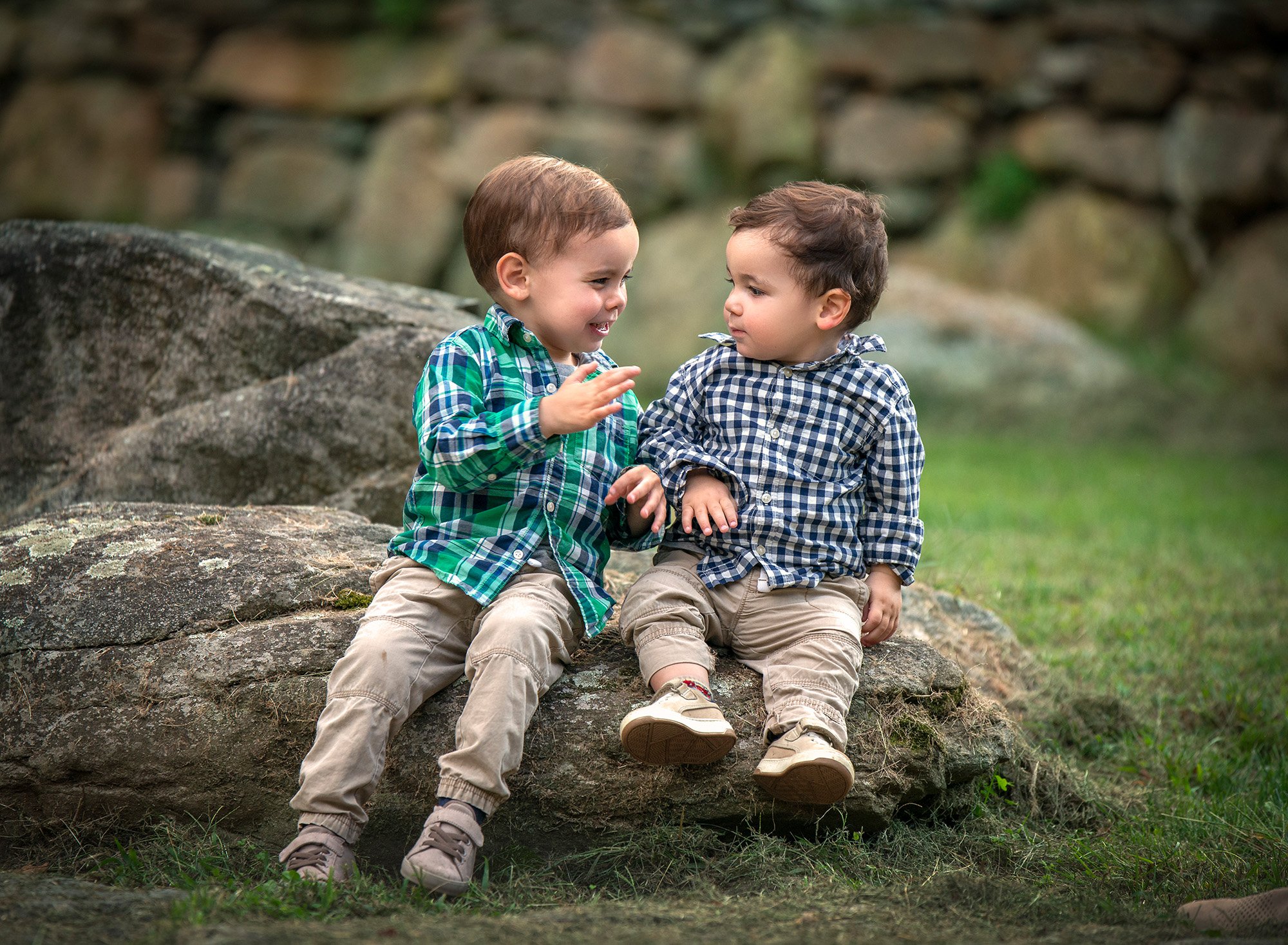 1 year old and family photography two young brothers looking at each other while sitting on a large rock in nature