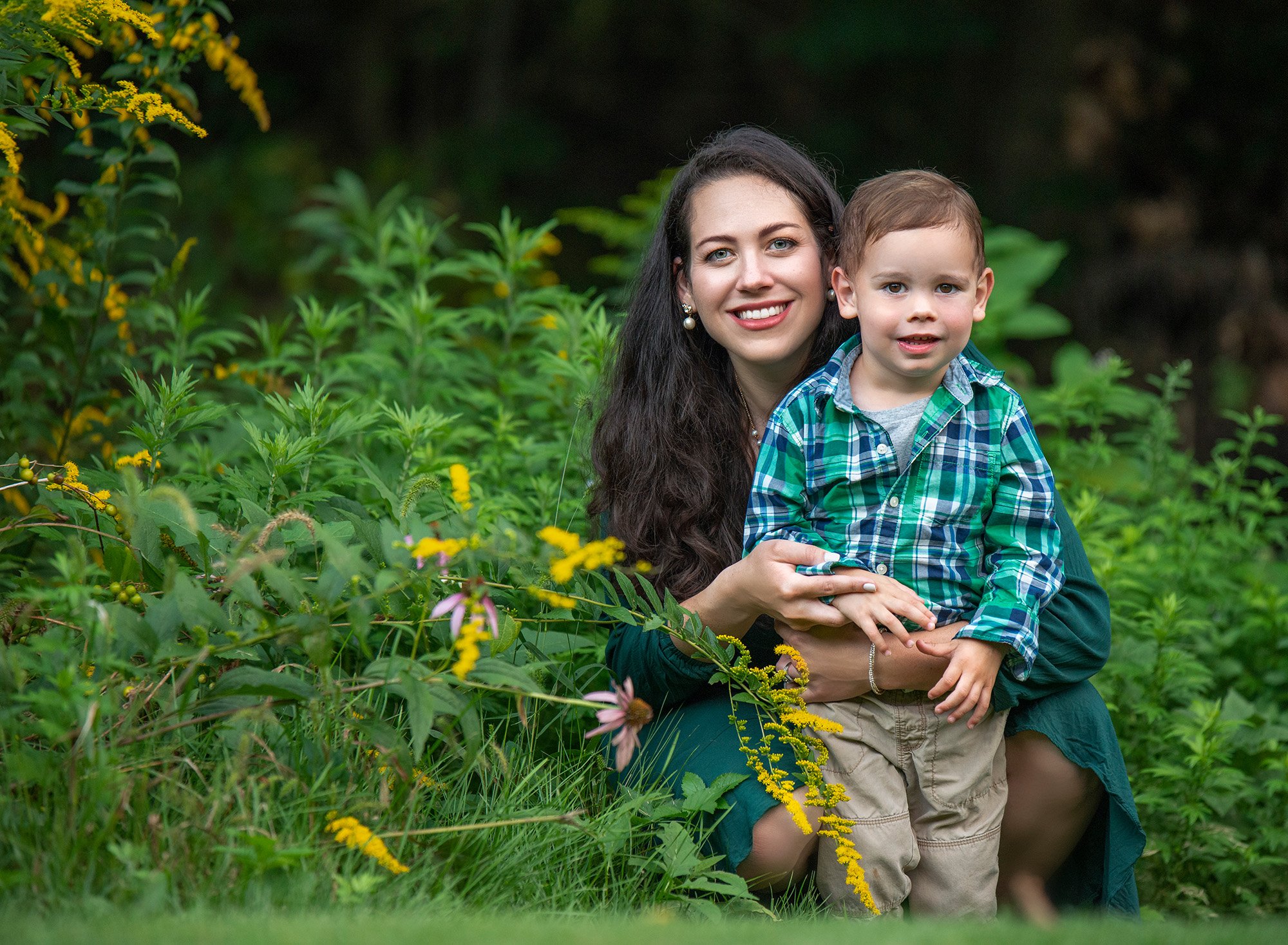 mom posing with one year old son in front of flower bush