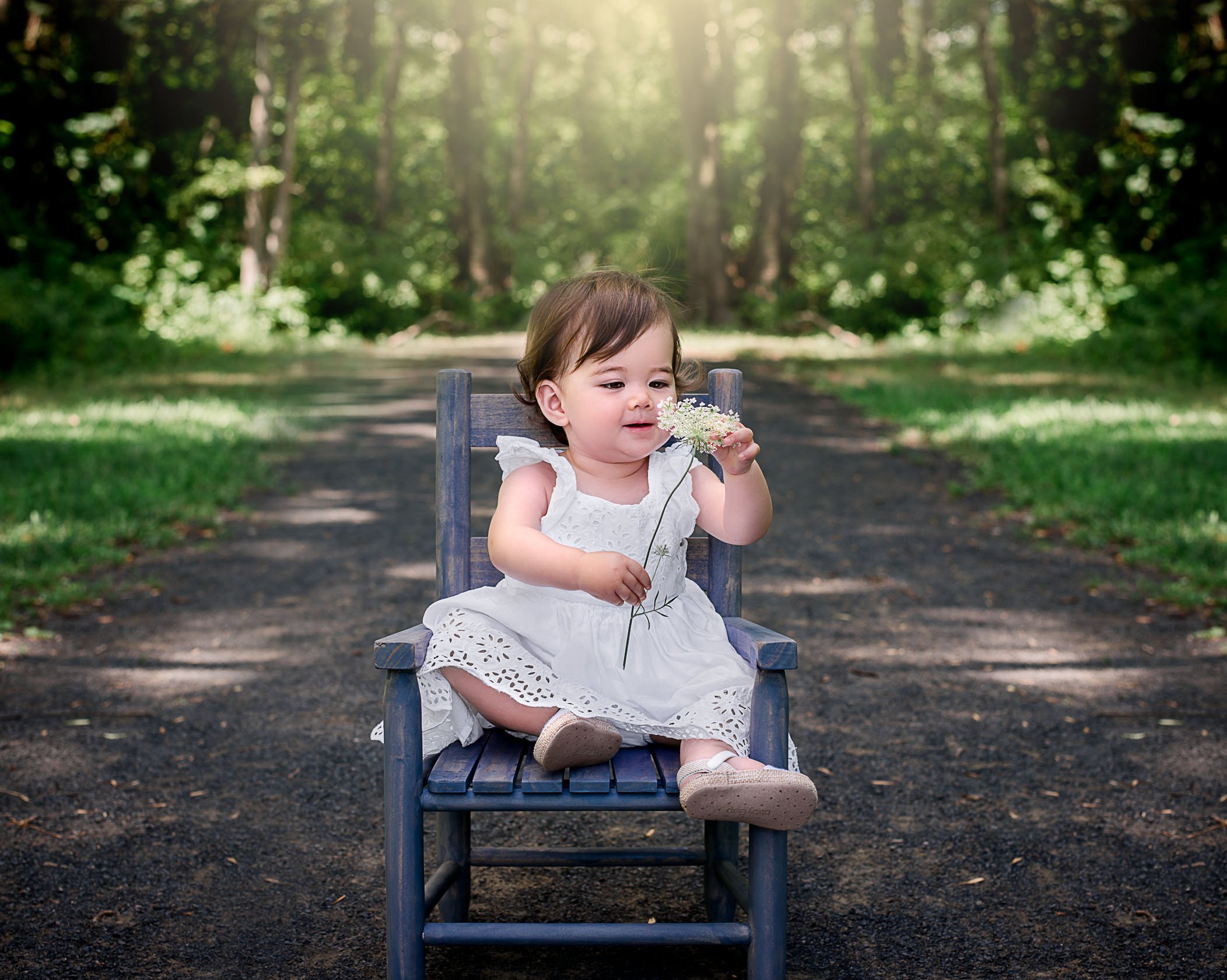 1 year old baby girl sitting in chair in garden playing with a flower One Big Happy Photo