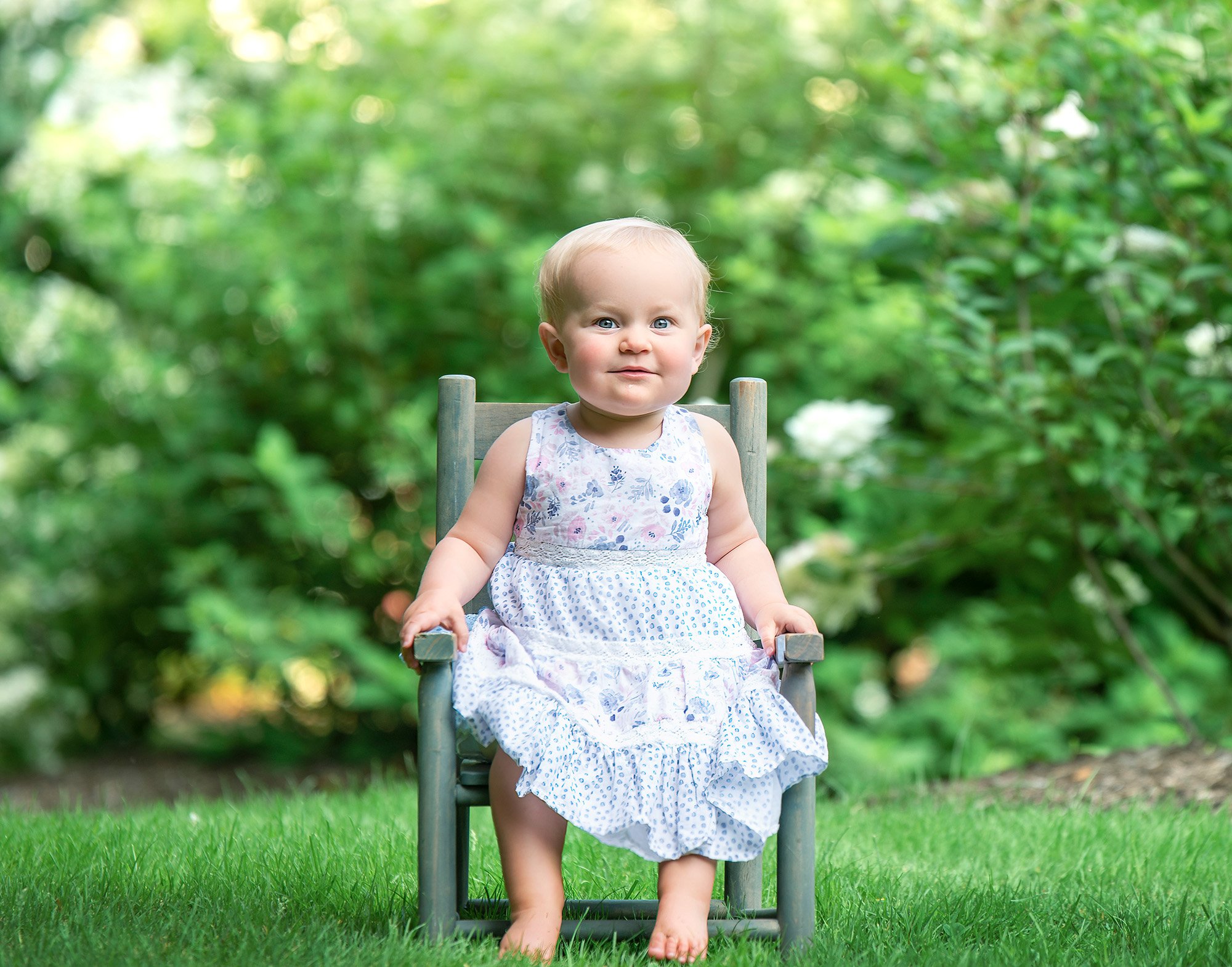 one year old little girl sitting on rustic chair in nature