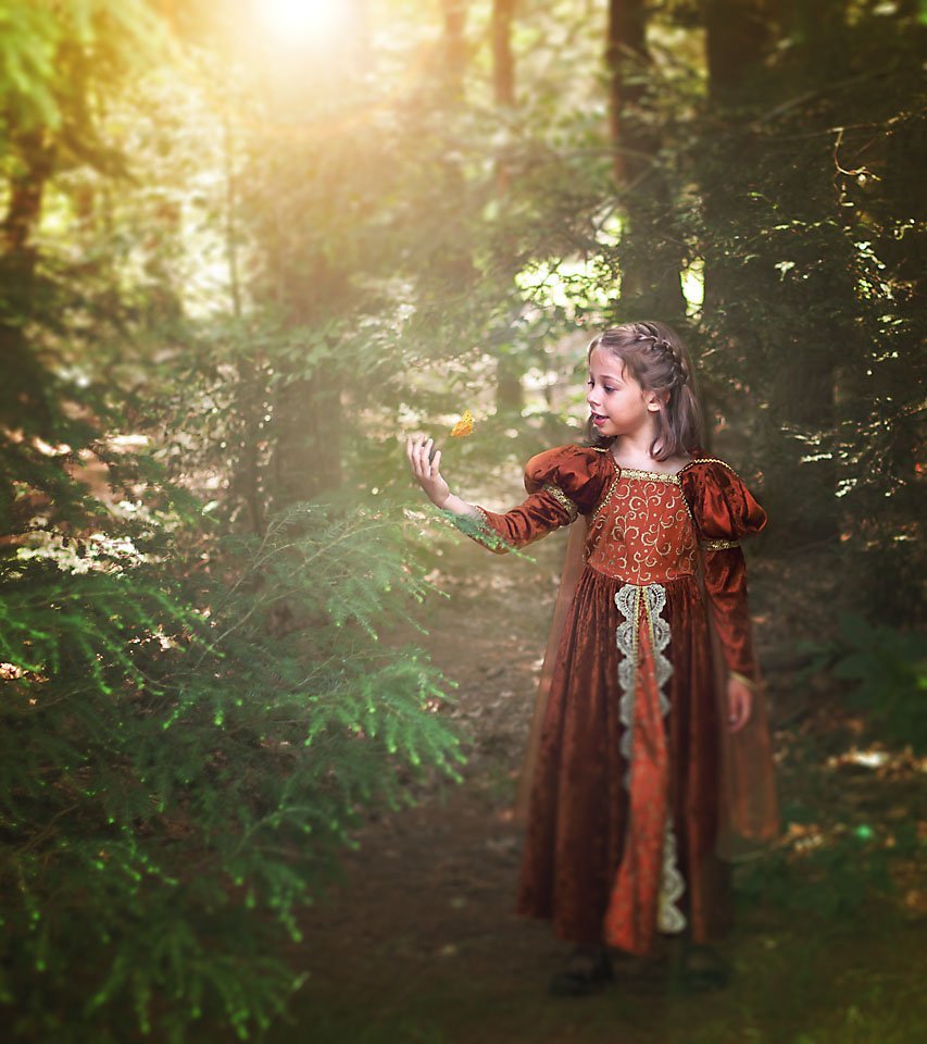 little girl walking in the forest with the sun shining behind her and an orange butterfly flies between her face and her hand