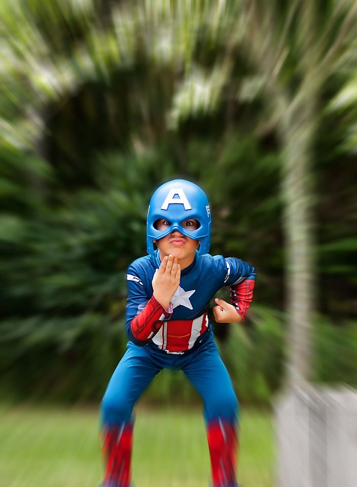 little boy dressed up as a superhero and about to take flight off of a railing in the forest