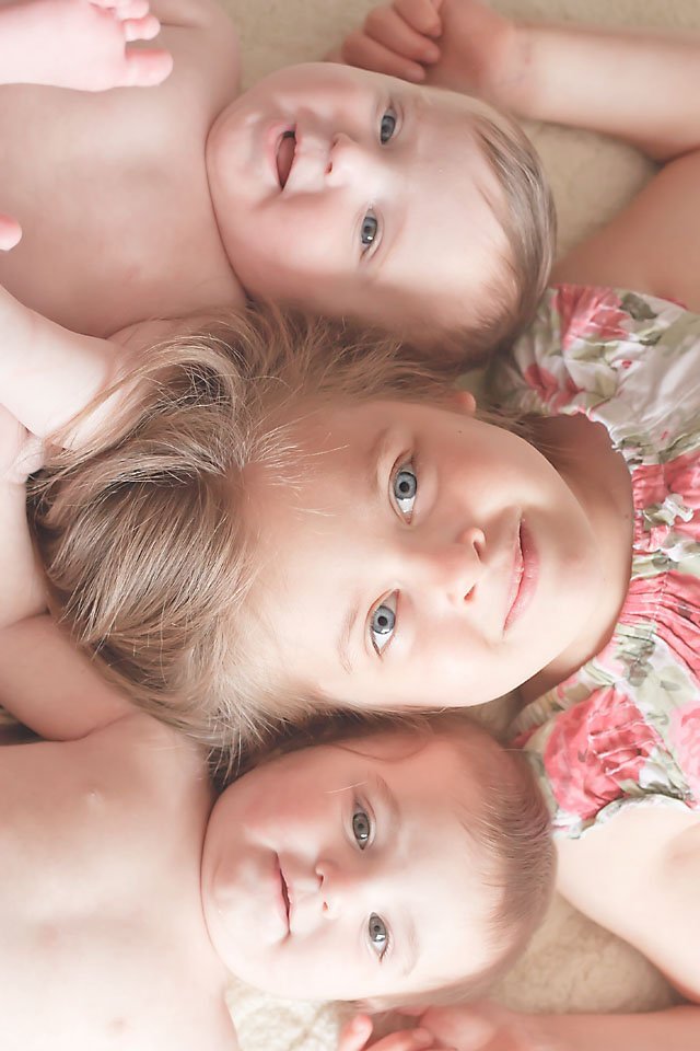 fraternal twins and their big sister lying on the floor with their heads all lined up and close together