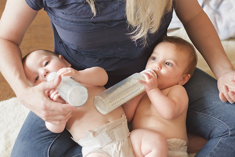 Fraternal twins, girl and boy, drinking bottles while nestled in their mother's lap