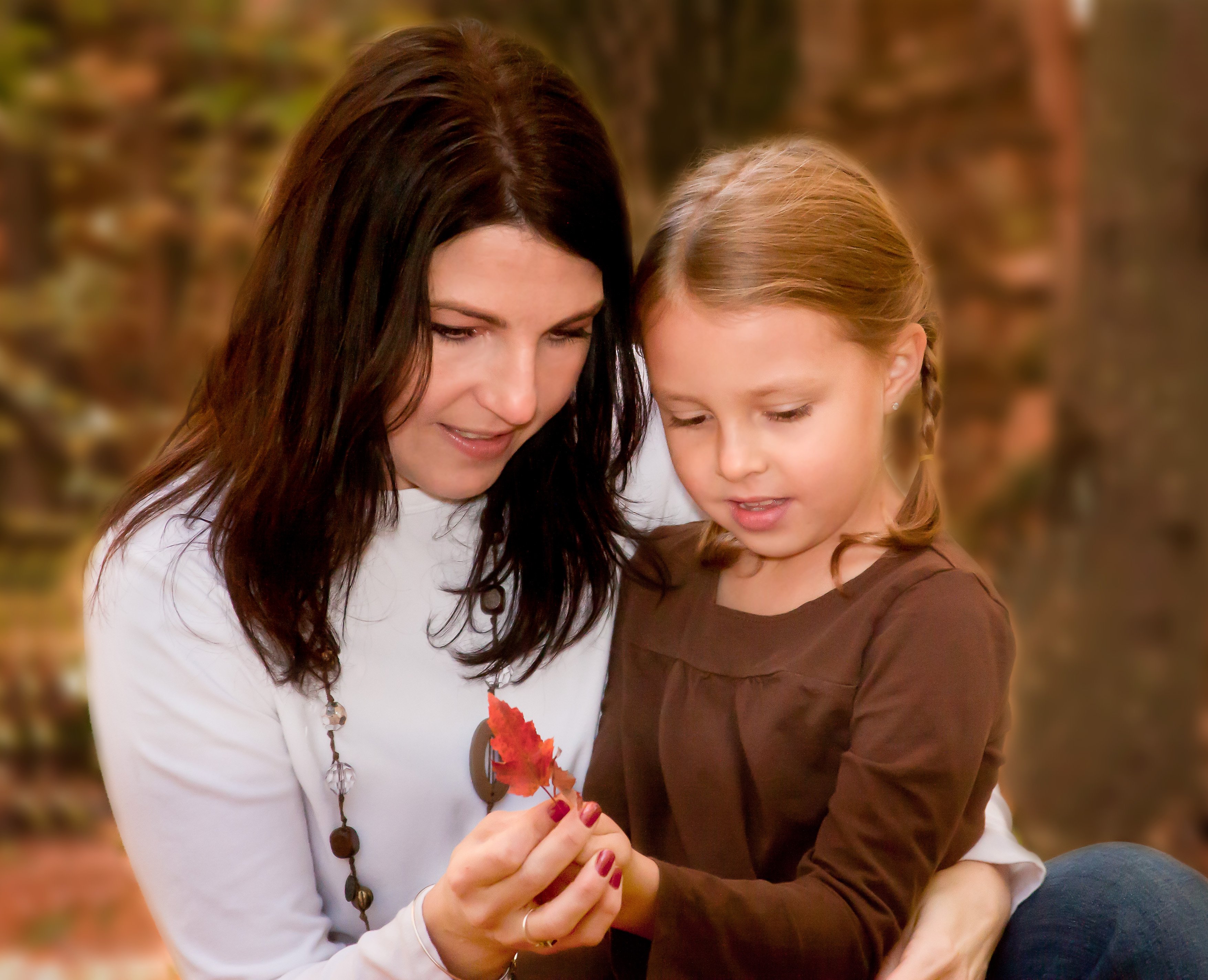 Mom and young daughter looking at a red fall leaf