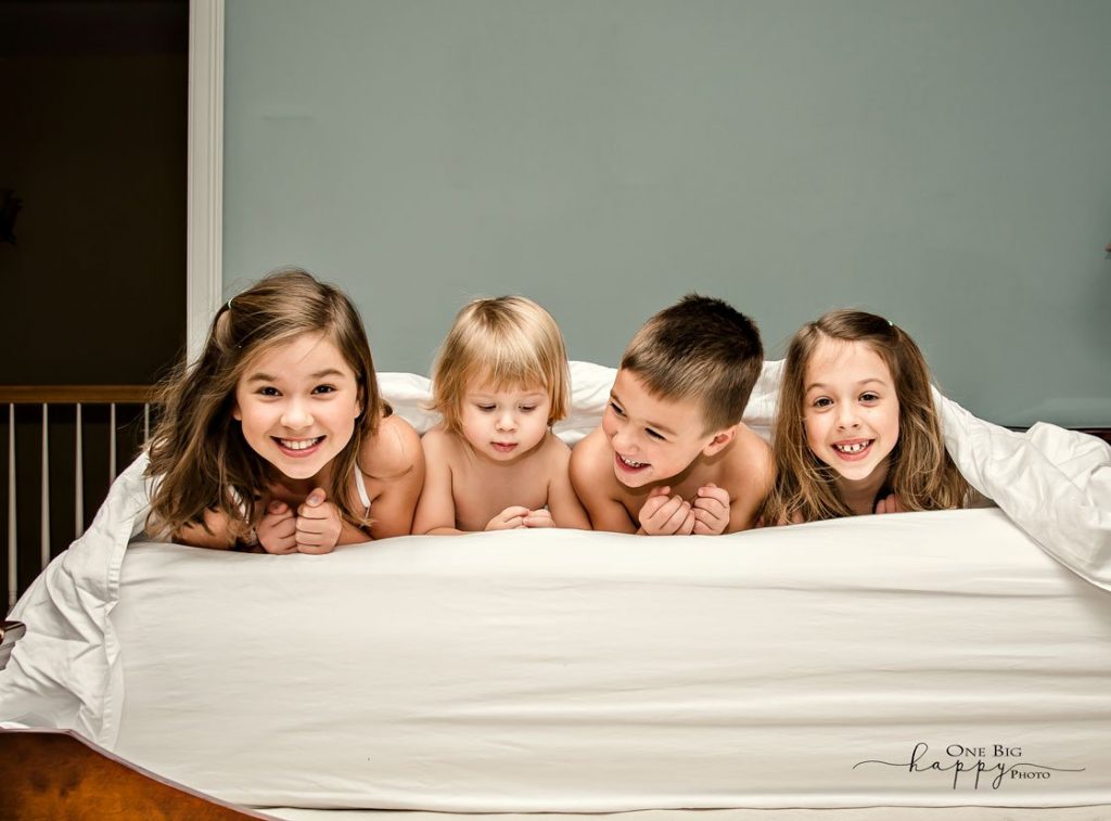 Four siblings lying across a bed smiling
