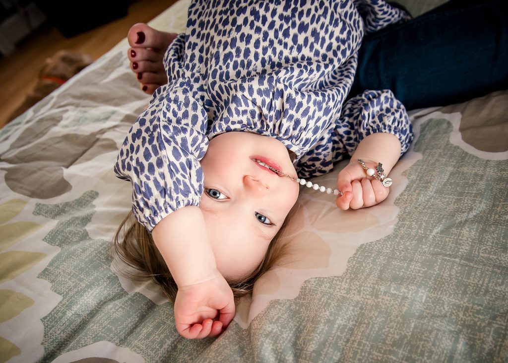 toddler girl chews on beaded bracelet while lying down