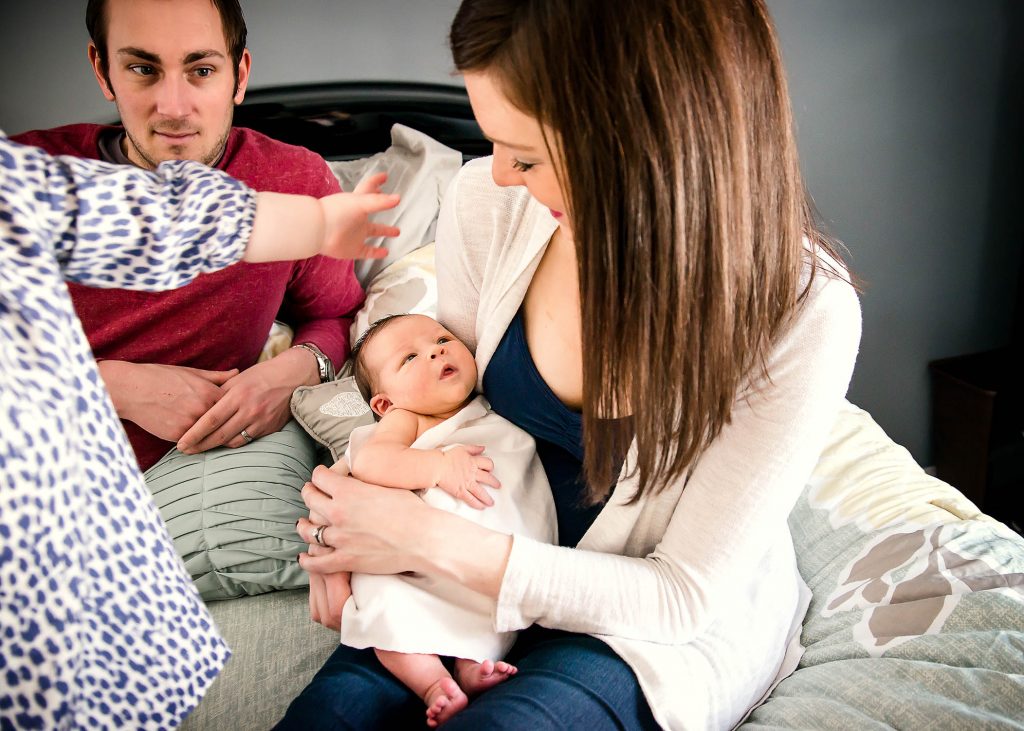 newborn baby staring up at mom while family sits on the bed