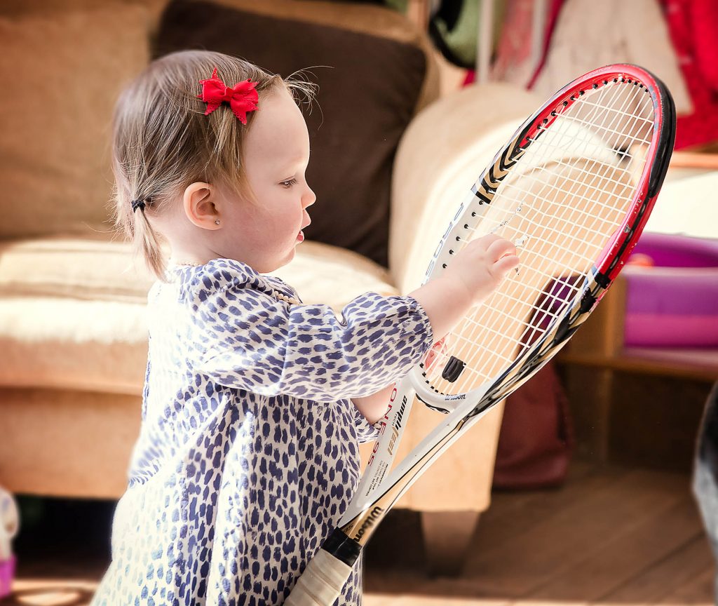 toddler hangs her tennis bracelet on her tennis racket