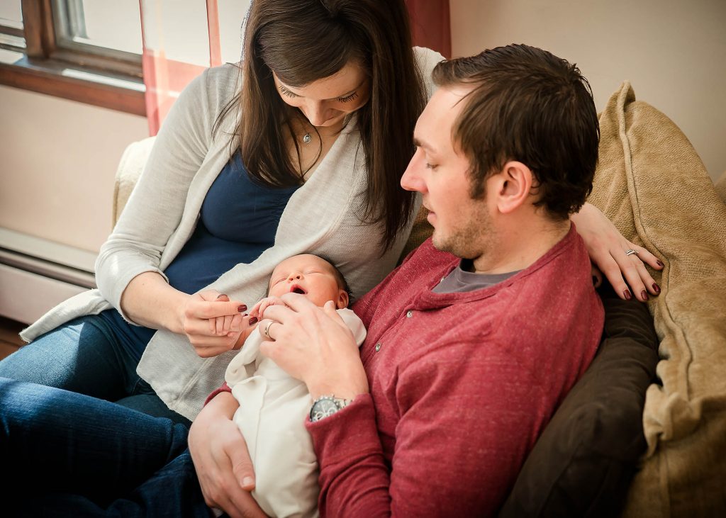 Mom, Dad and newborn daughter share a cuddle on the couch