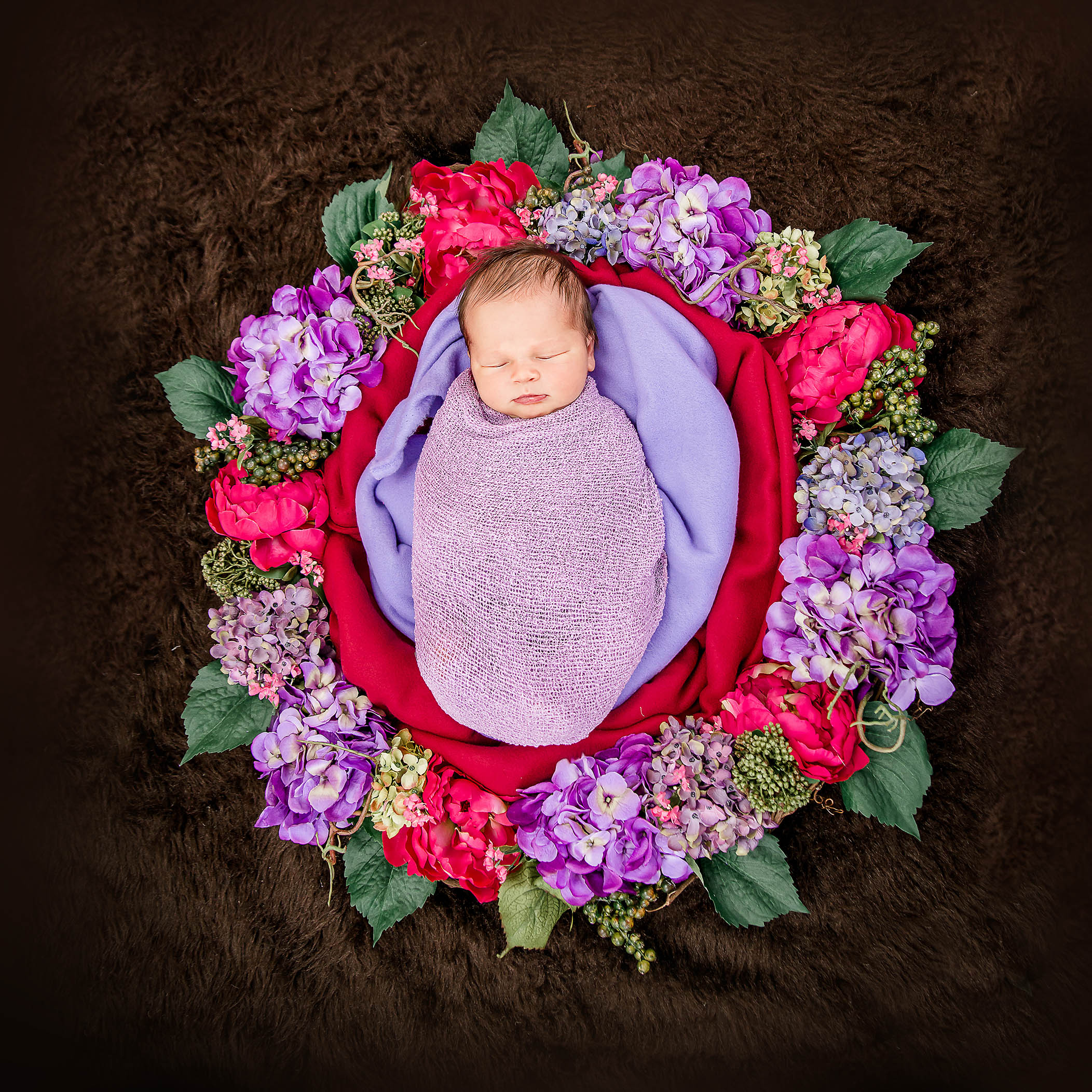 4 day old newborn girl swaddled in a floral wreath of dark pink and lavender flowers