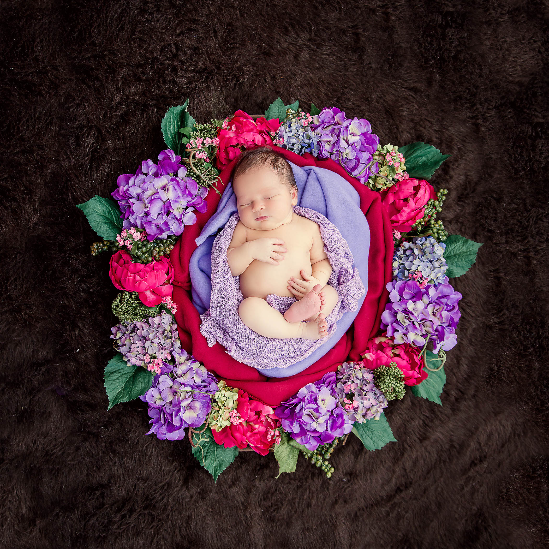 Newborn girl sleeping naked in a floral wreath of dark pink and lavender flowers
