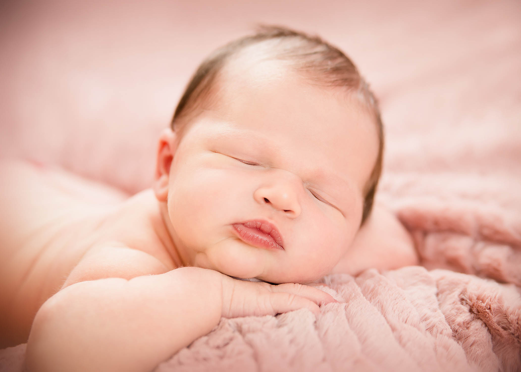 newborn baby girl lying on pink blanket with lips pursed